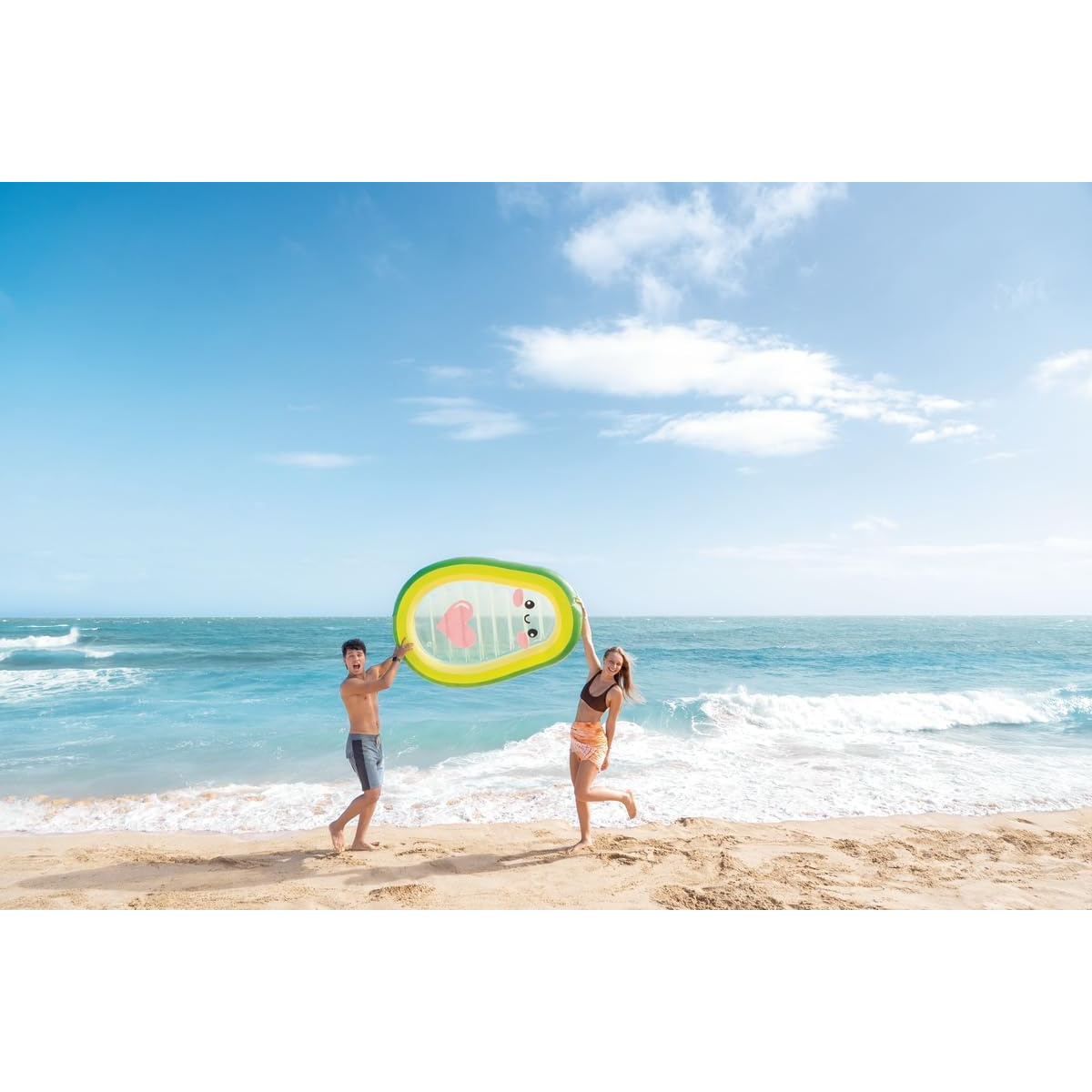 Mann und Frau halten auf einem Sandstrand einen aufblasbaren Avocado-Schwimmring.