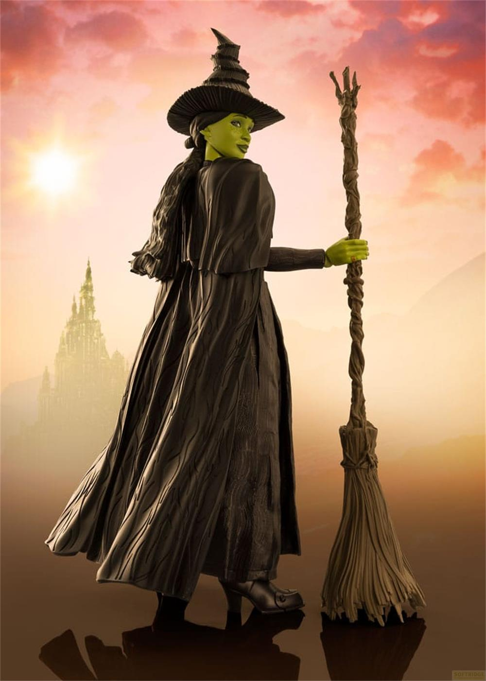 Grüne Hexe mit Hut und Besen vor einer Burg im Sonnenuntergang.