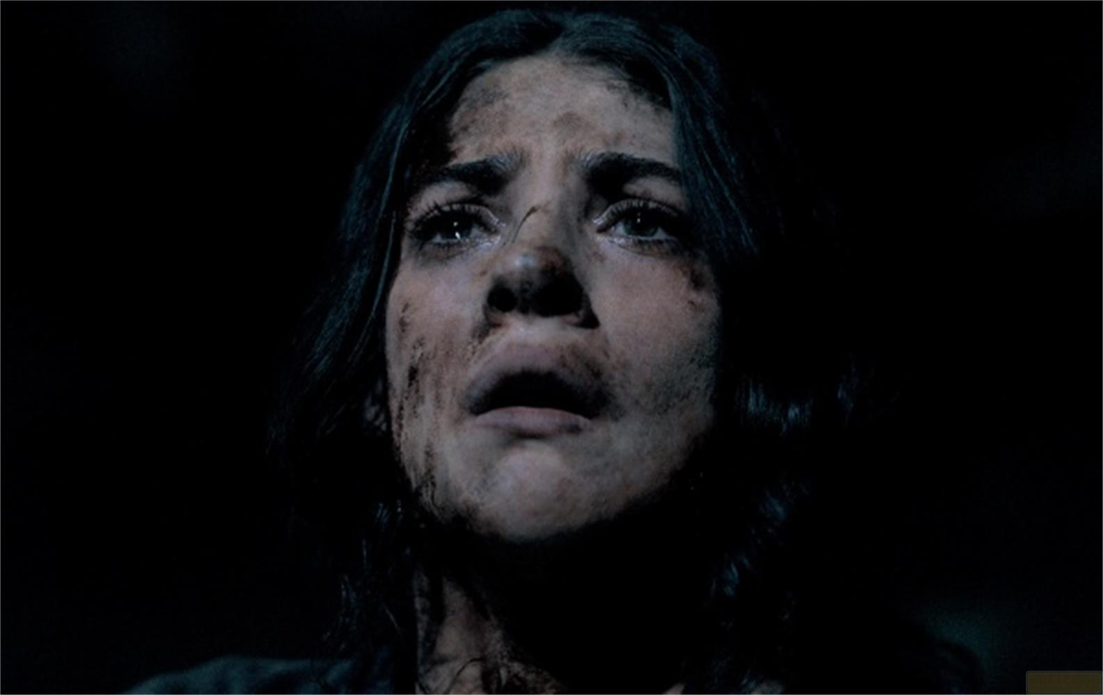 Una giovane donna con il viso sporco alza lo sguardo con le lacrime agli occhi.