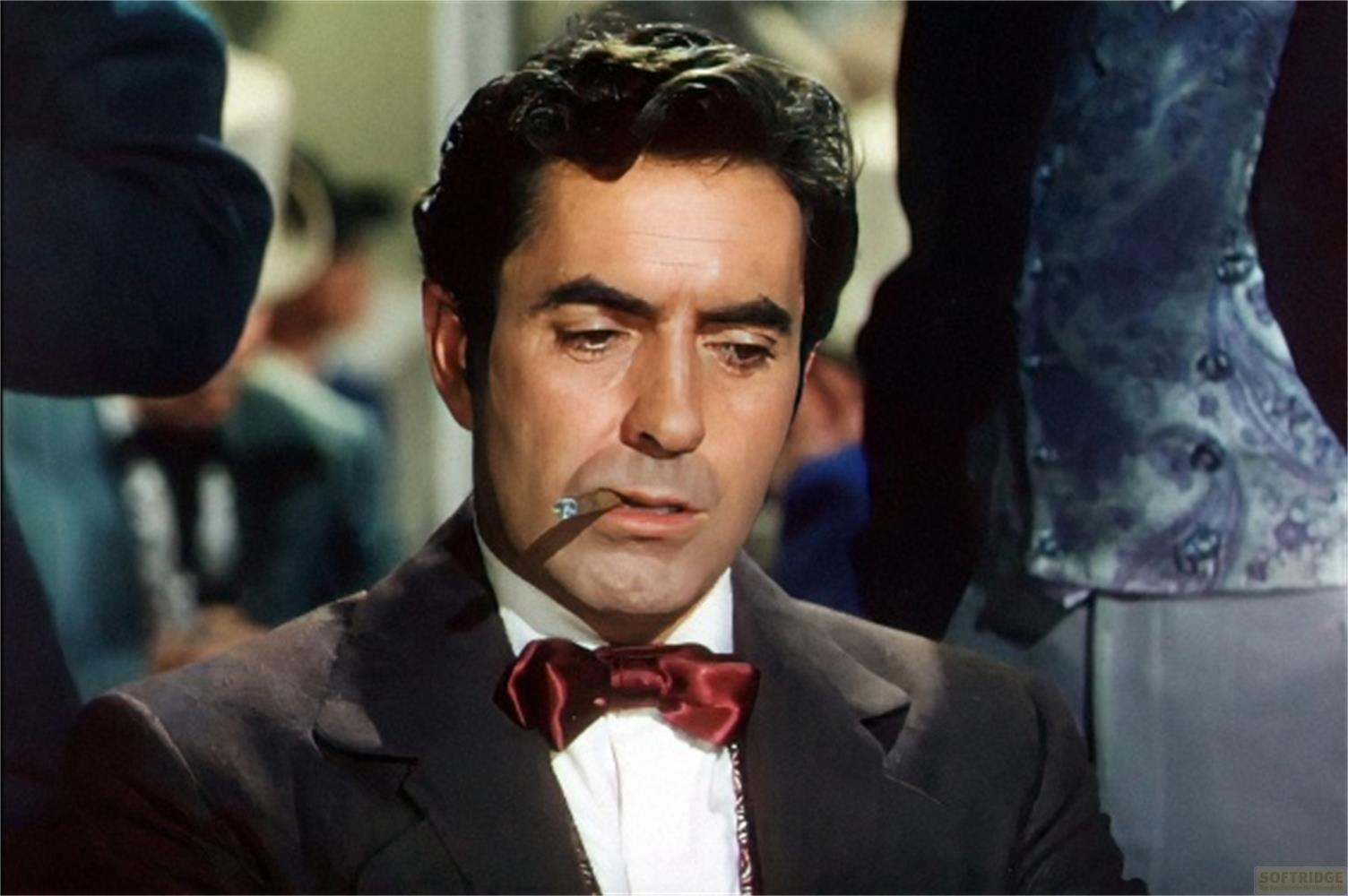 Un uomo con capelli scuri e papillon fuma una sigaretta.