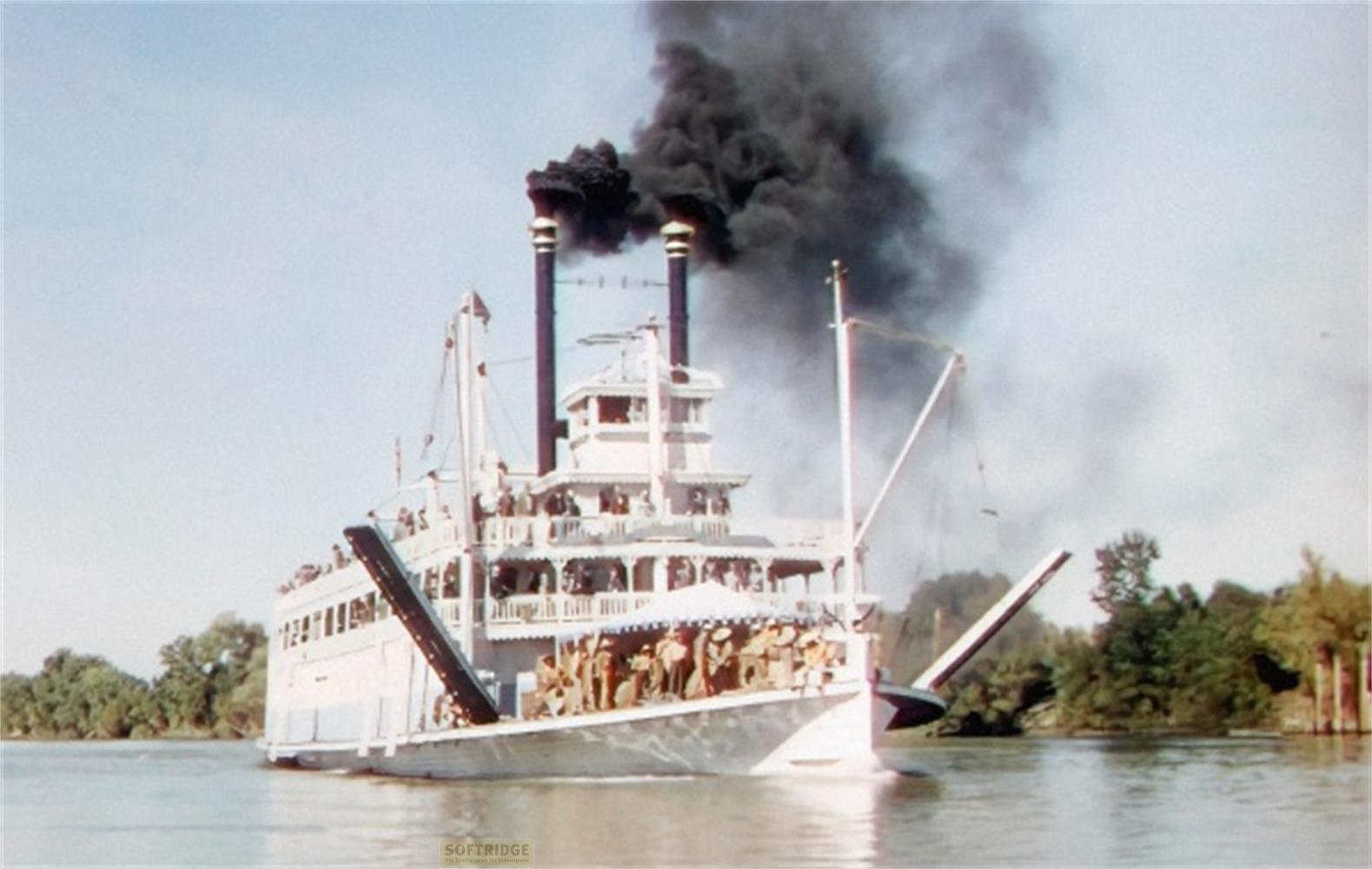 Un battello a vapore bianco con fumo nero esce dai suoi fumaioli su un fiume.