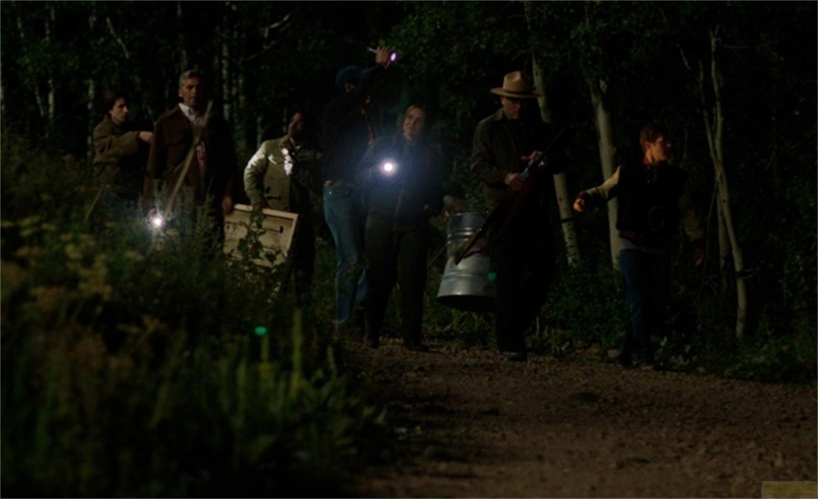 Un gruppo di persone cammina su un sentiero nel bosco di notte, alcuni con torce.