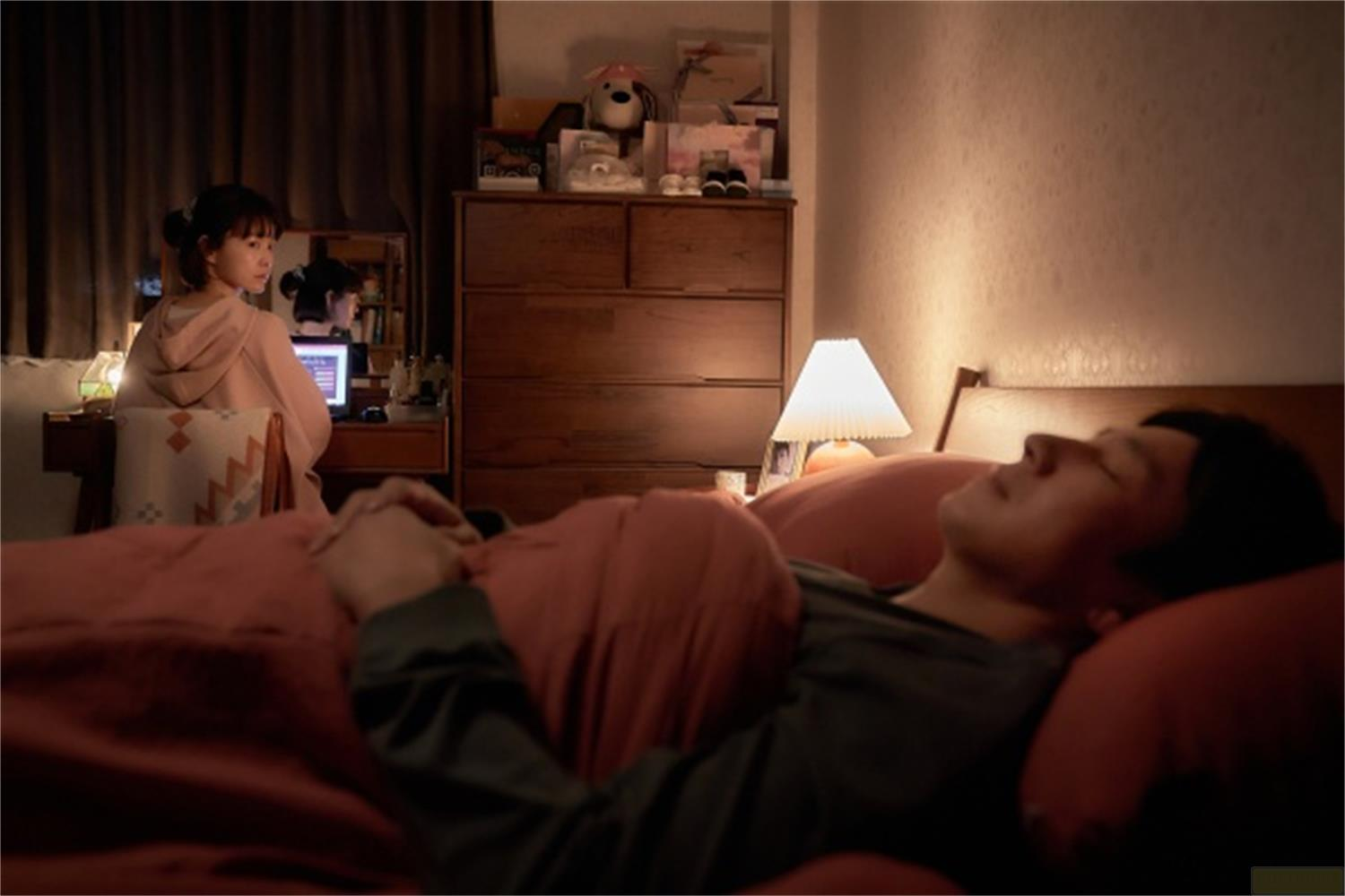 Un uomo dorme a letto mentre una donna è seduta a una scrivania.