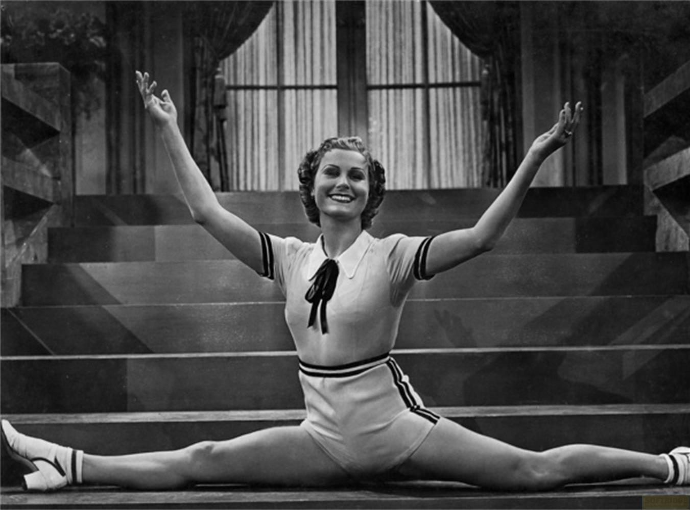 Donna in abiti sportivi fa la spaccata sulle scale, sorride con le braccia alzate.