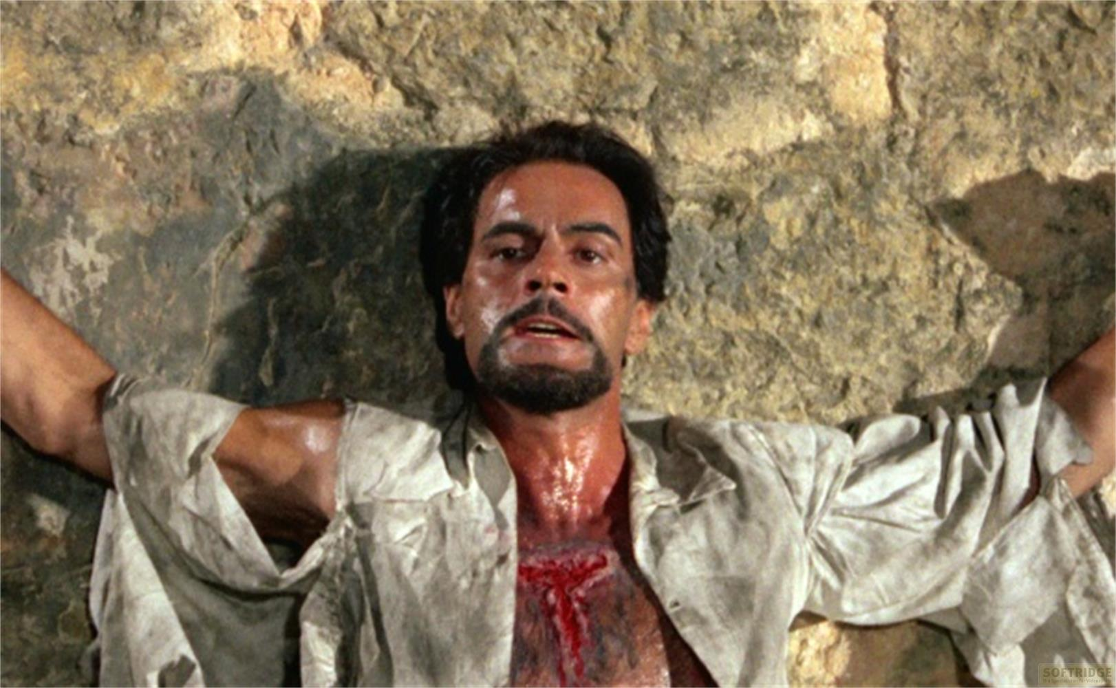 Un uomo con la barba giace contro una parete rocciosa, il petto ferito.