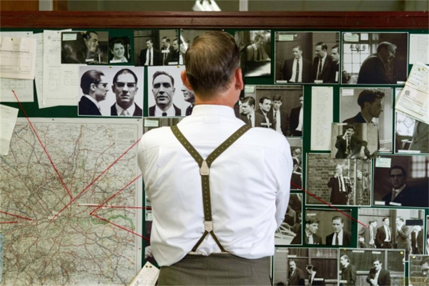 Uomo con bretelle guarda mappa e foto su bacheca.