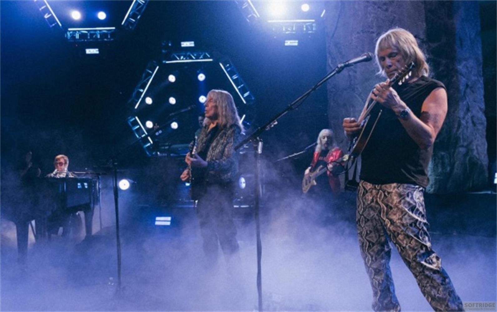 Musiker spielen auf einer Bühne mit Nebel und blauer Beleuchtung.