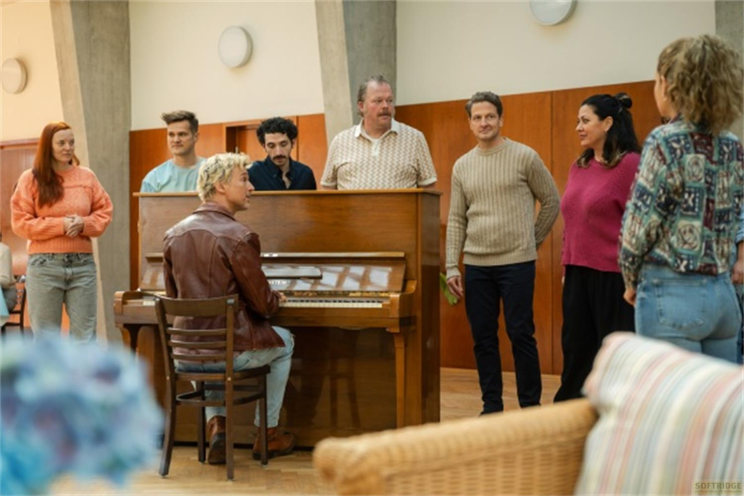 Un gruppo di persone attorno a un pianoforte, una persona suona.