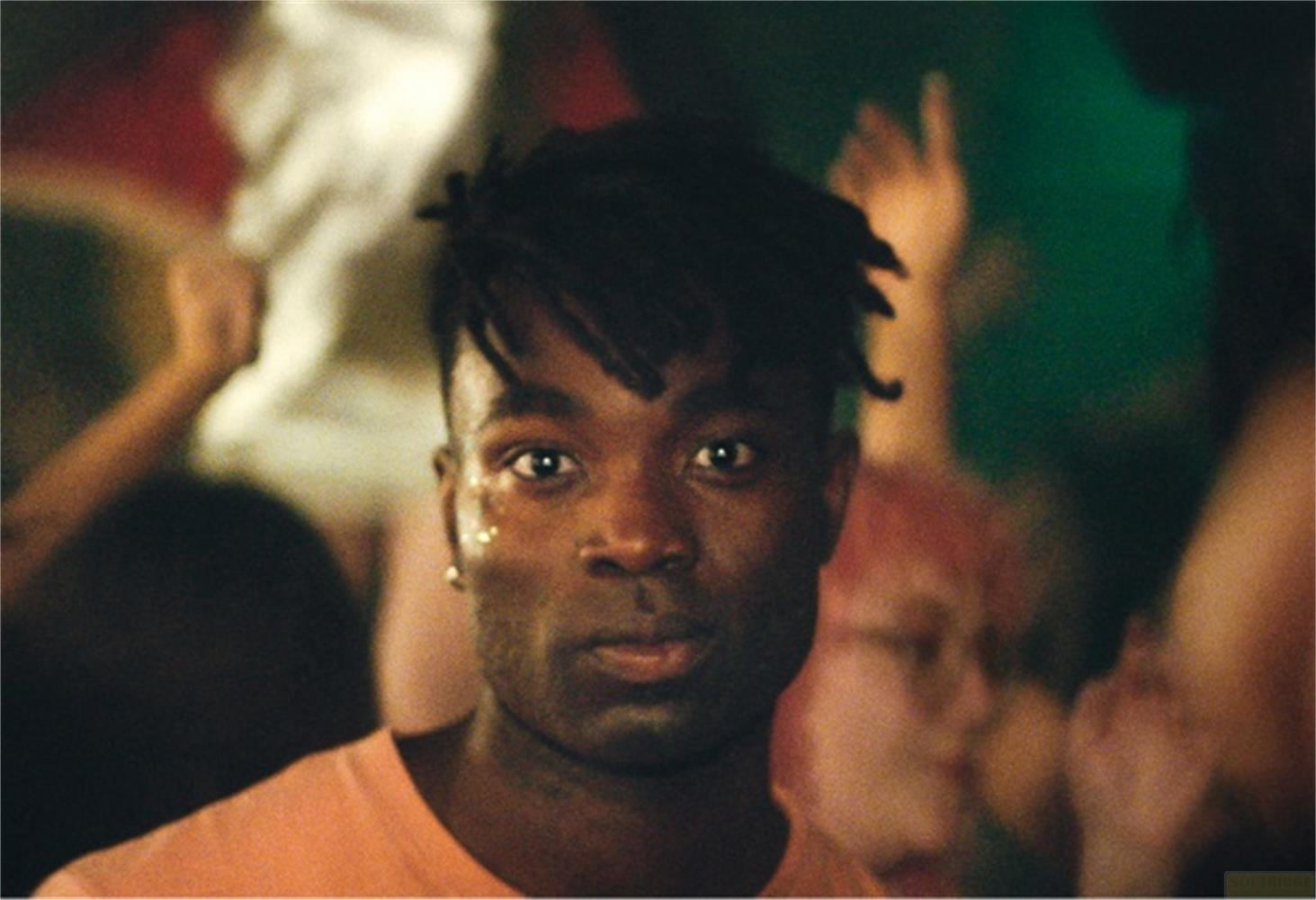 Ein junger Mann mit Dreadlocks und Glitzer im Gesicht blickt in die Kamera.