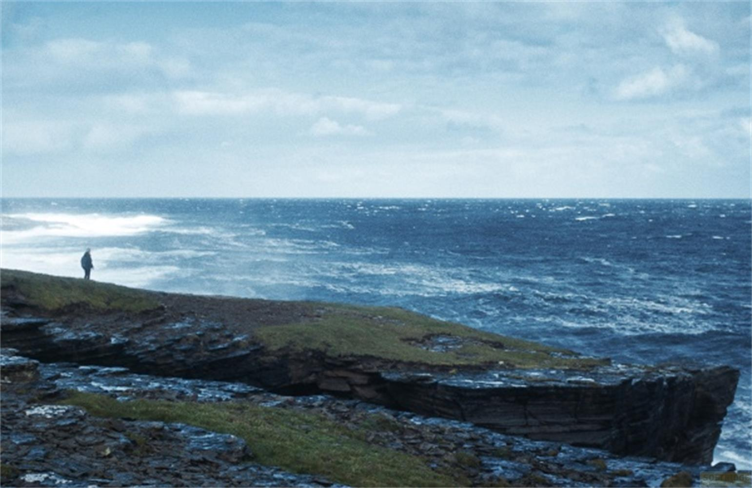 Eine Person steht auf einer felsigen Klippe am Meer.