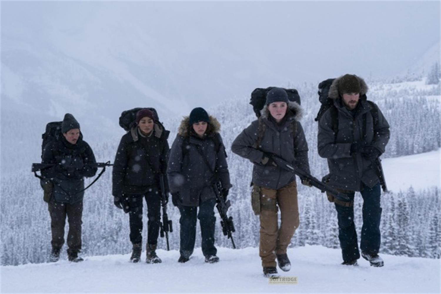 Fünf Personen in Winterkleidung wandern durch verschneite Berge, bewaffnet mit Gewehren.