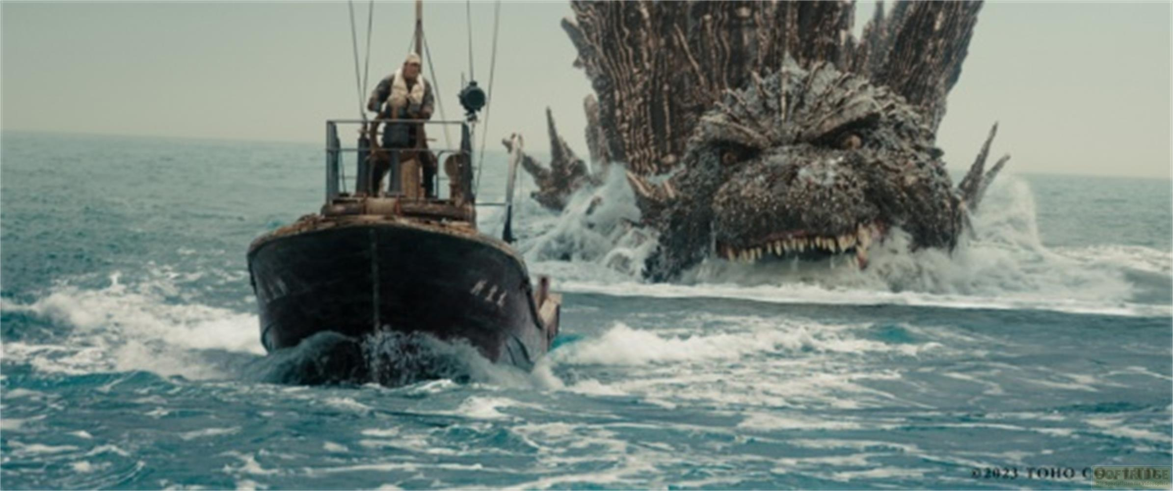 Ein Fischerboot fährt auf dem Meer, während Godzilla aus dem Wasser auftaucht.