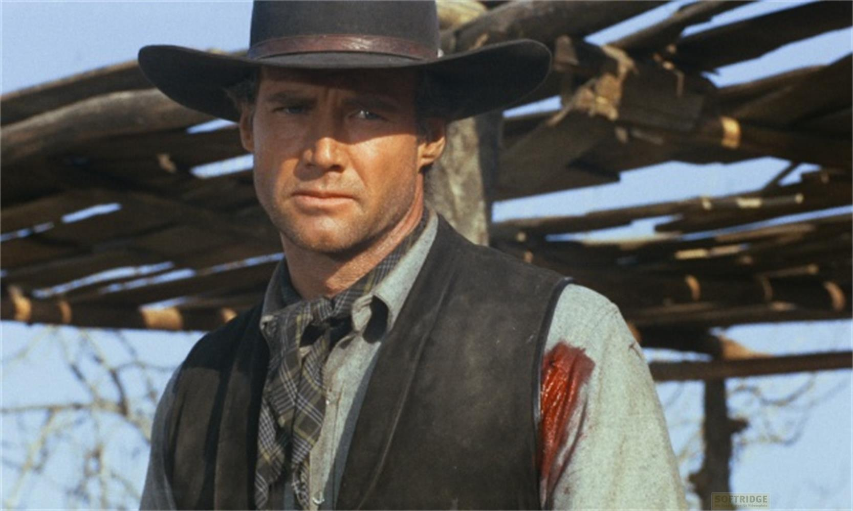 Un uomo in abiti western con cappello e gilet, i suoi vestiti sono insanguinati.