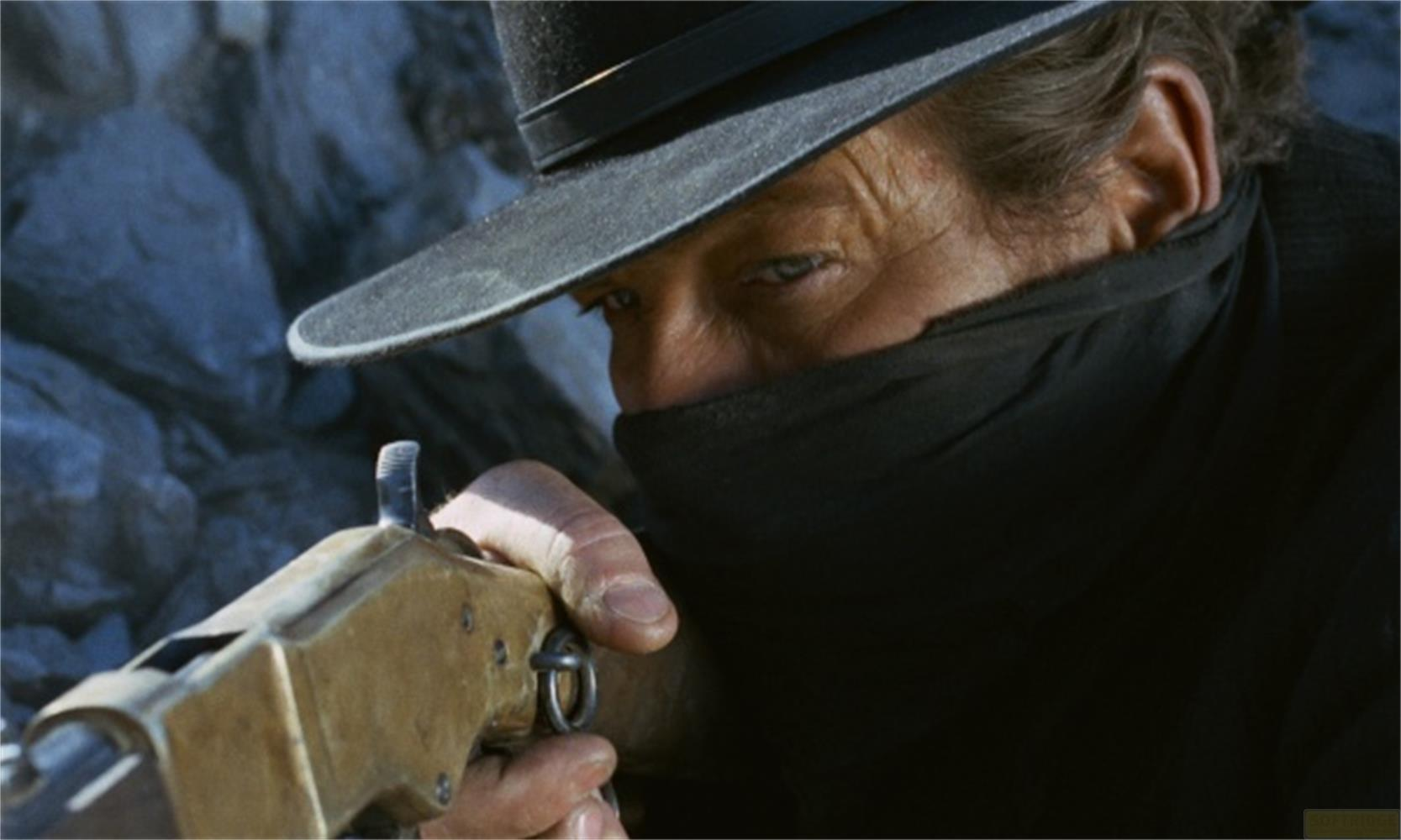 Uomo con cappello e sciarpa punta fucile verso rocce.