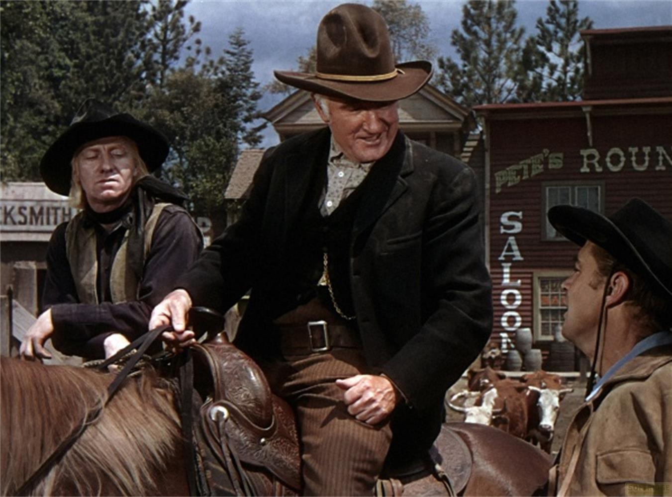 Tre cowboy a cavallo in una città western. Un uomo ride.