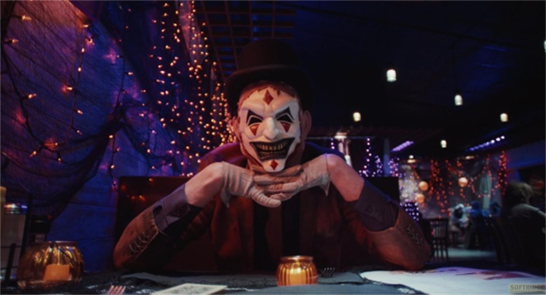 Una persona con maschera da clown siede a un tavolo decorato con luci.