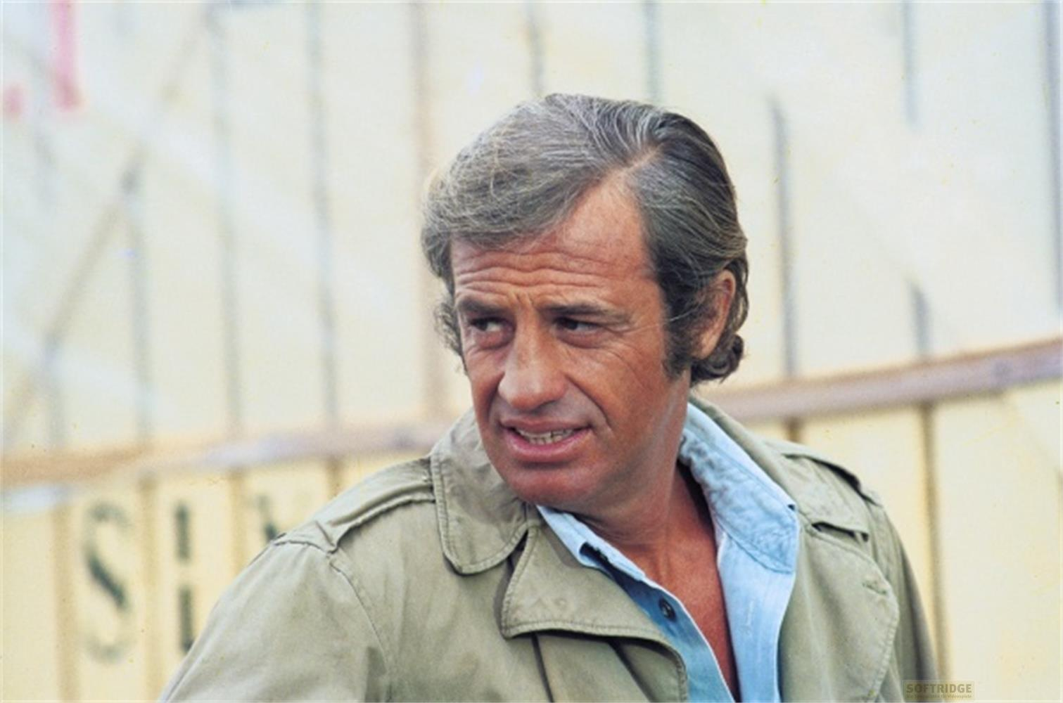 Uomo con capelli grigi in giacca kaki e camicia blu, guarda a sinistra.