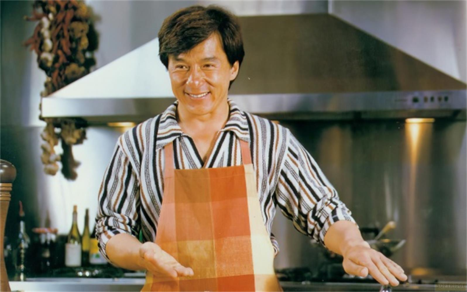 Jackie Chan in einer Küche mit Schürze und gestreiftem Hemd.