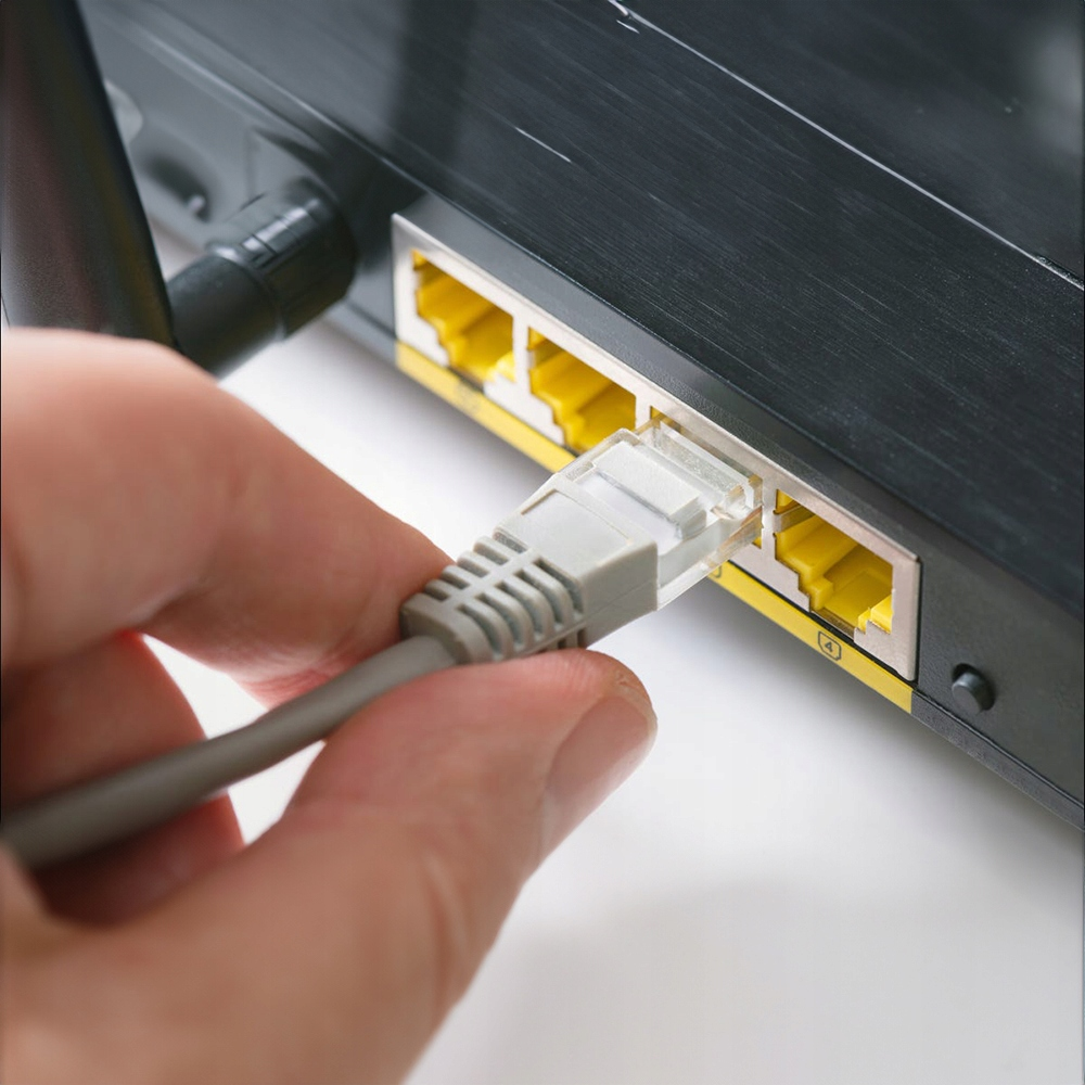 Ręka podłącza szary kabel sieciowy do czarnego routera.