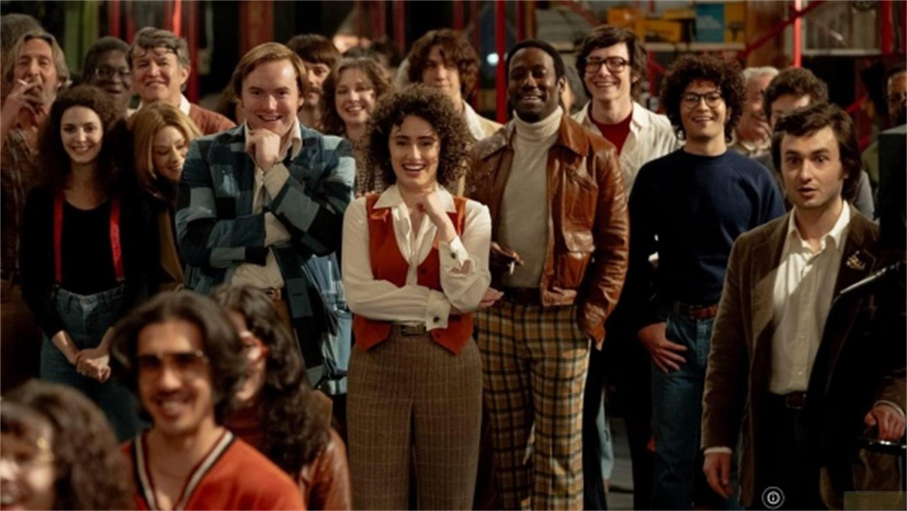 Un gruppo di persone in abiti anni '70 sta insieme sorridendo.