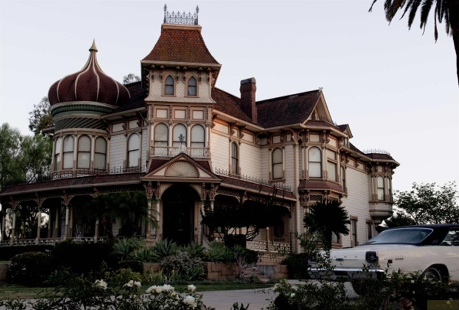 Una grande casa vittoriana con torrette, portici e un'auto d'epoca.