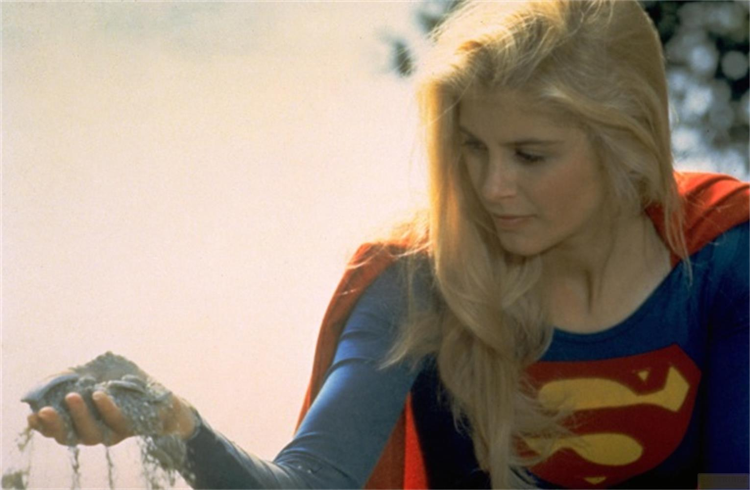 Una donna in costume da Supergirl tiene sabbia tra le mani. Ha i capelli biondi.