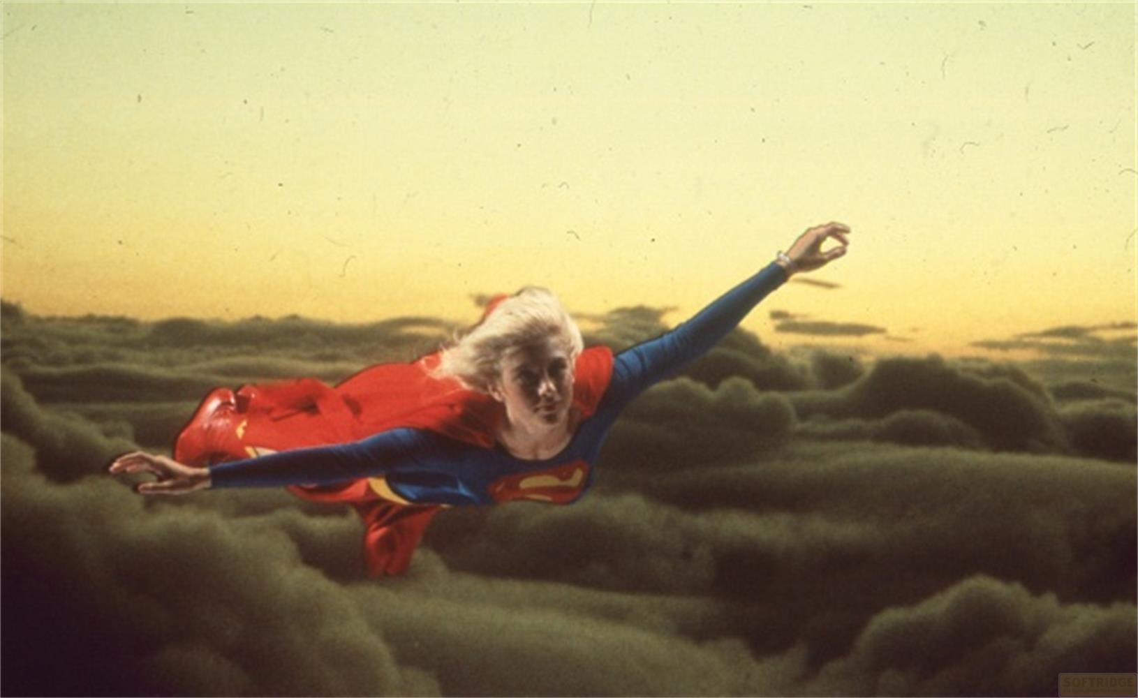 Una donna in costume da supereroina vola tra le nuvole al tramonto.