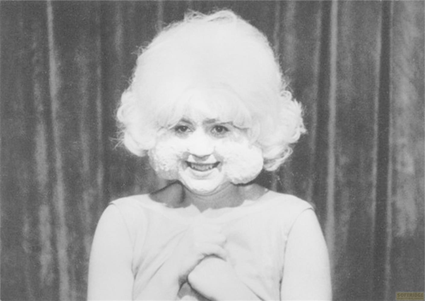 Una donna con parrucca bianca voluminosa e trucco bianco sorride.