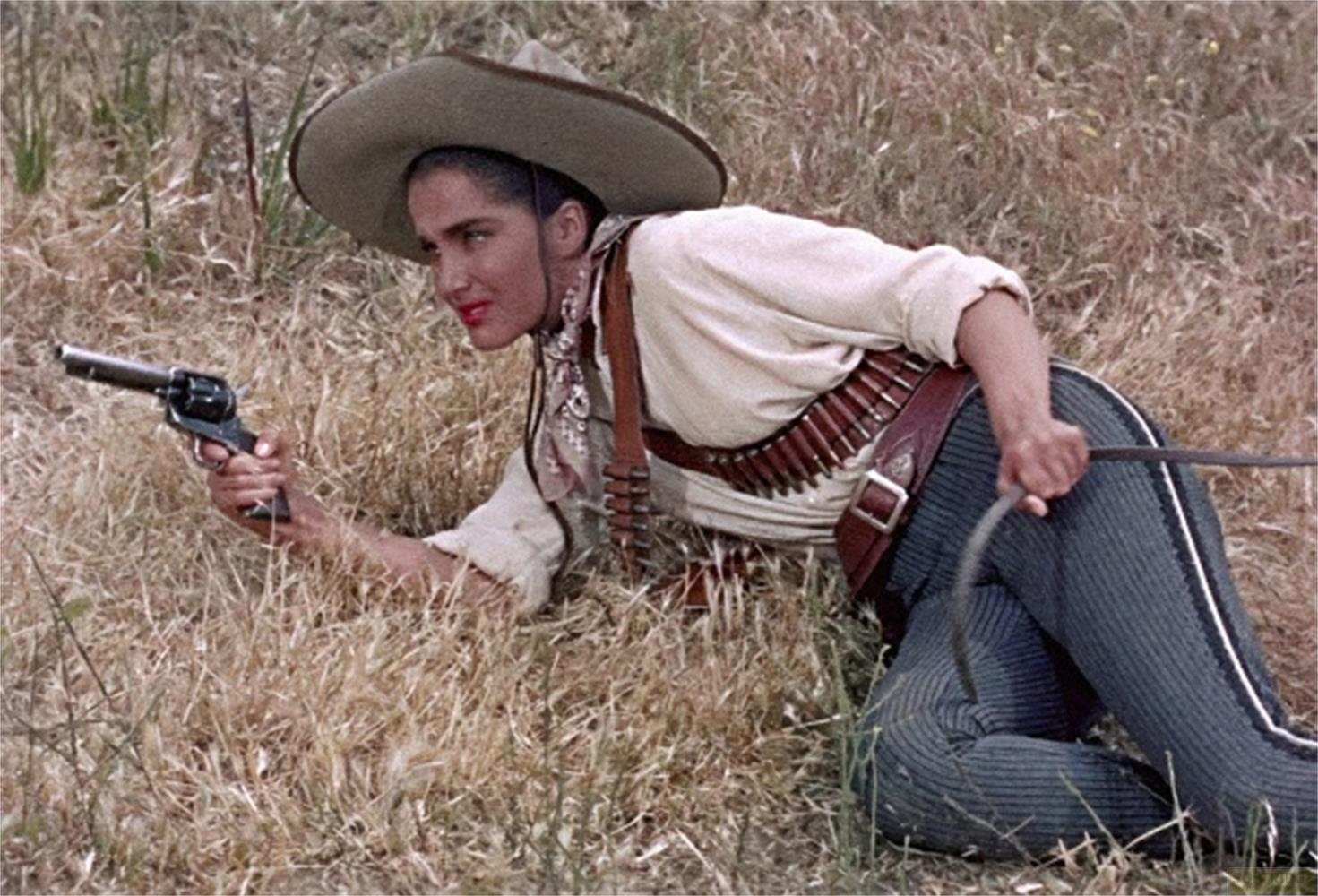 Donna con sombrero e rivoltella nell'erba alta, cintura porta munizioni in vita.