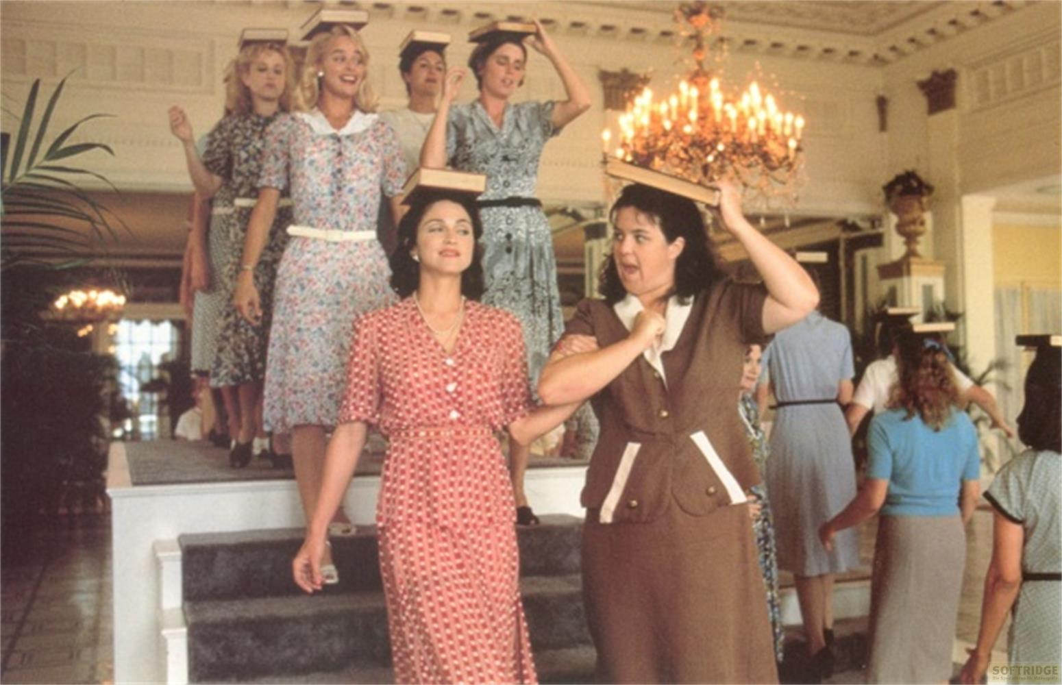 Frauen balancieren Bücher auf ihren Köpfen in einem eleganten Raum.