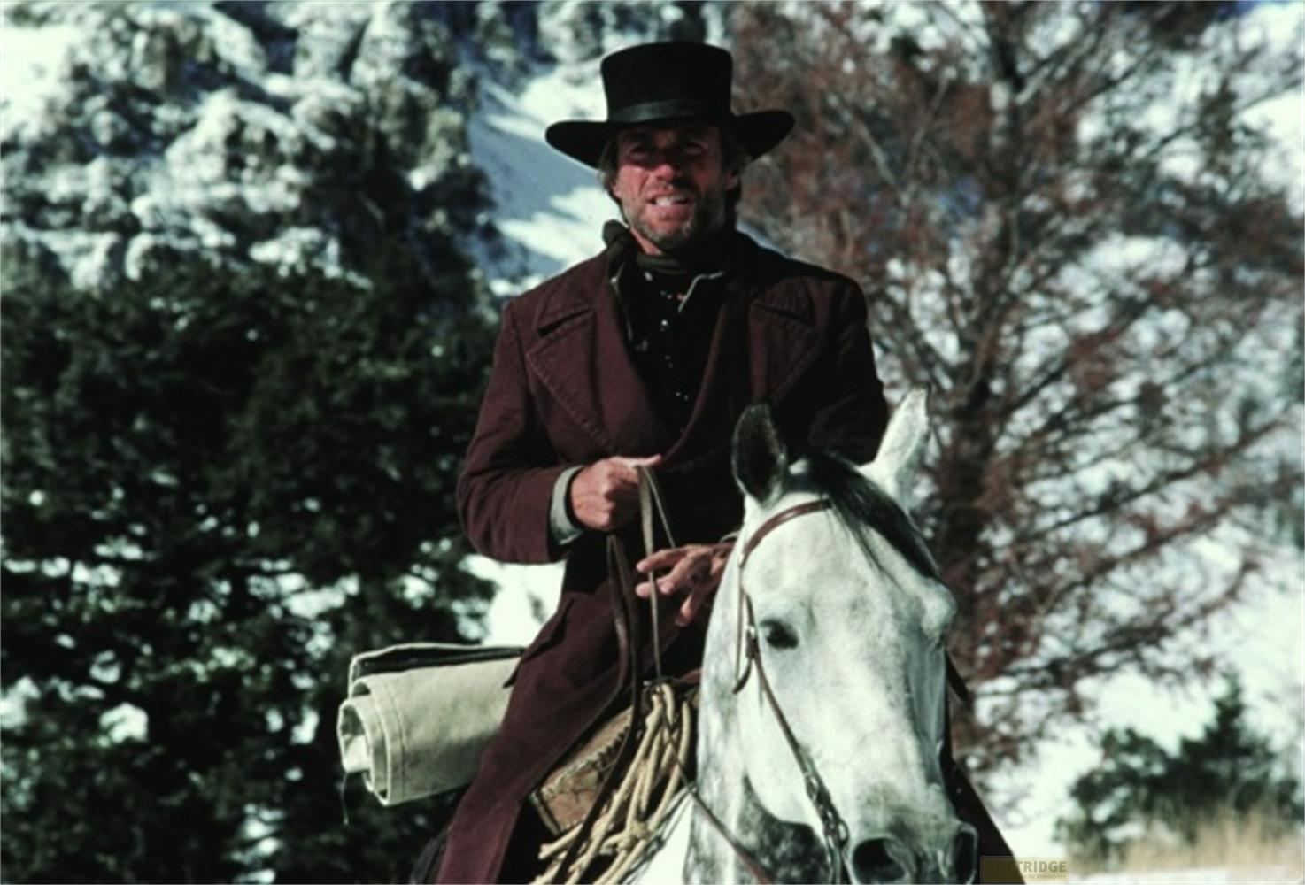 Un uomo in abiti scuri e cappello a cilindro cavalca un cavallo bianco nella neve.