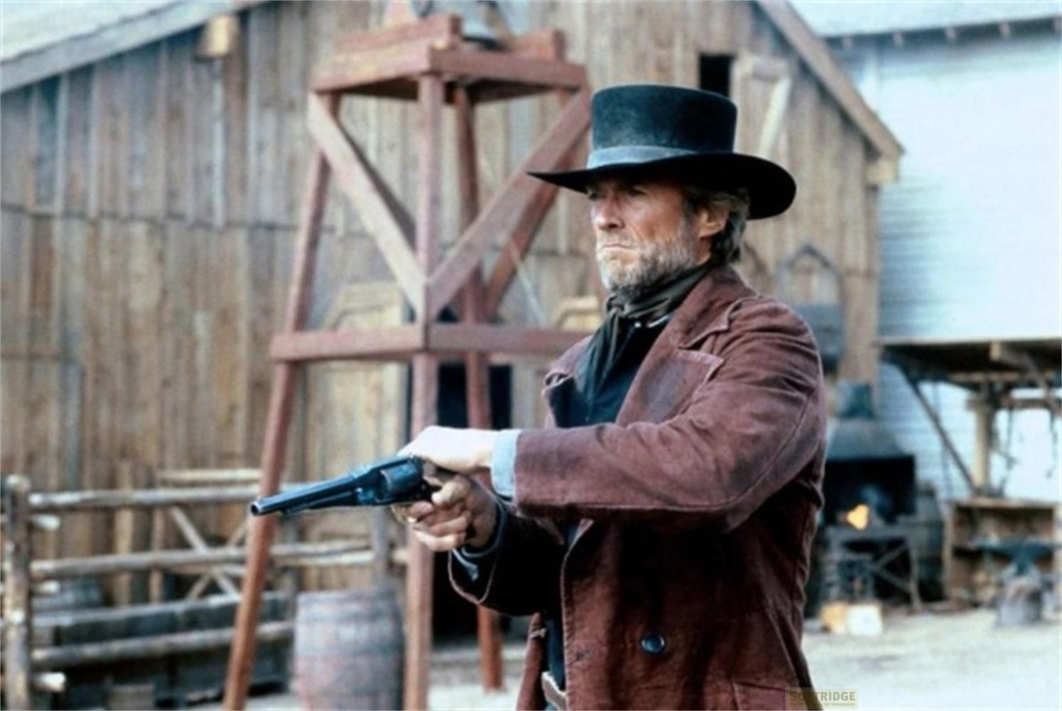 Un uomo con cilindro e cappotto marrone tiene una pistola, ambientazione western.