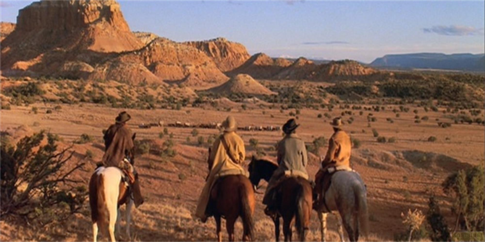 Quattro cavalieri guardano un vasto paesaggio desertico con montagne sullo sfondo.