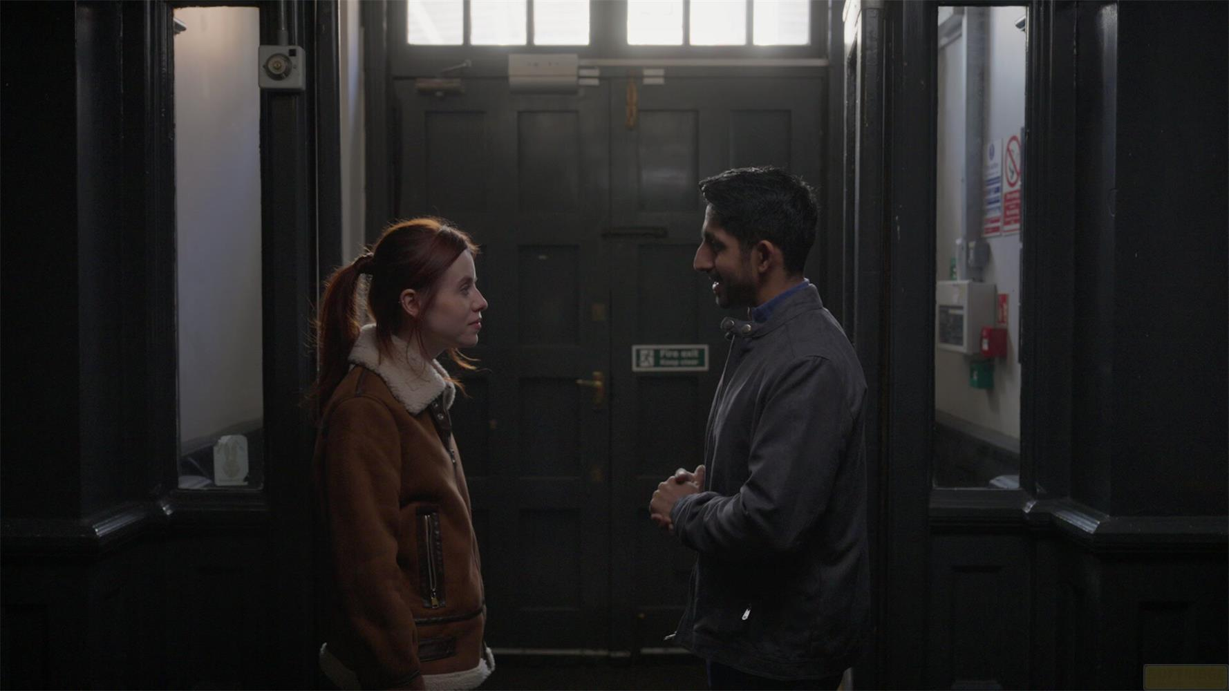 Un homme et une femme se font face devant une porte sombre.
