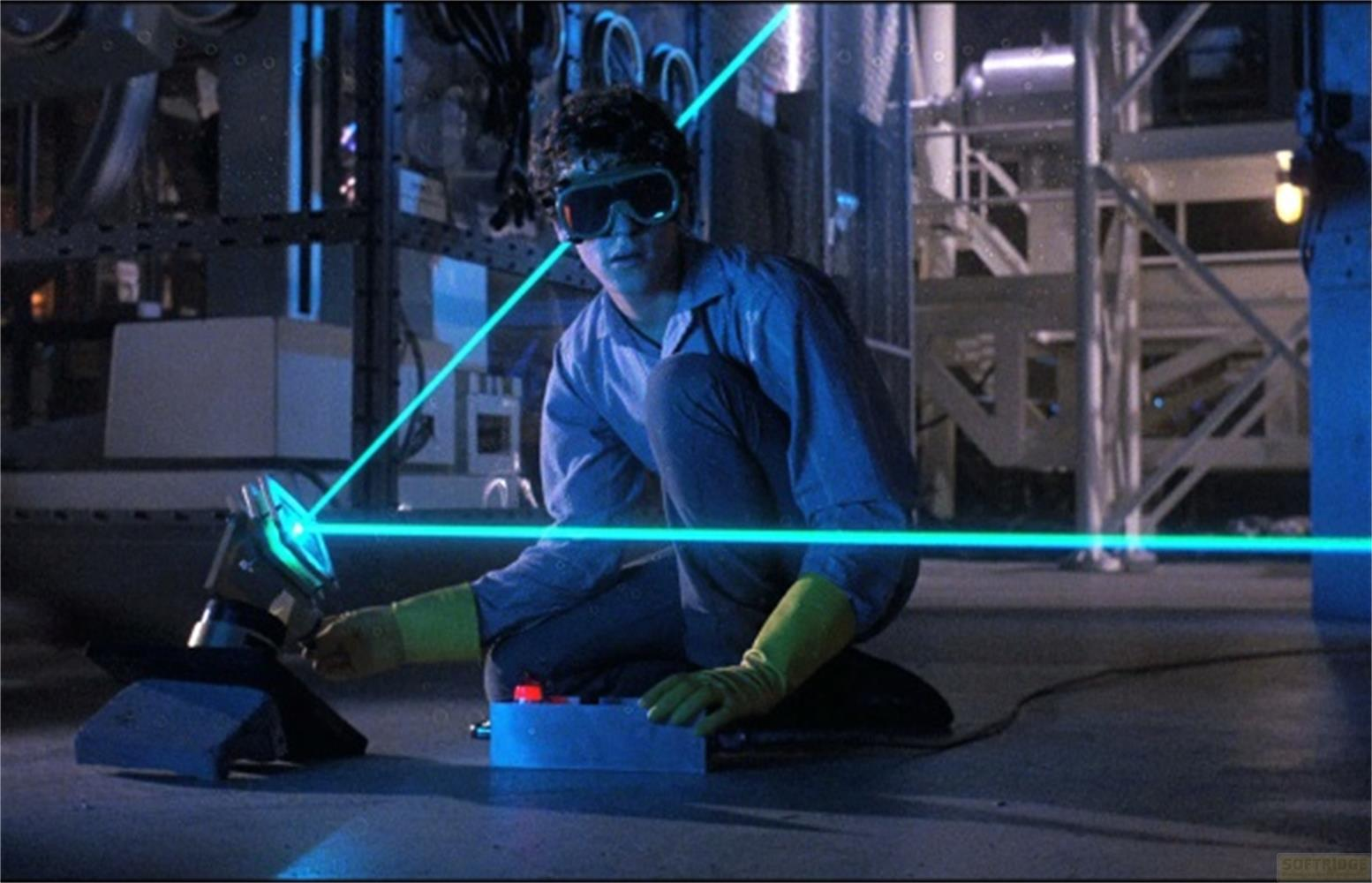 Un uomo in tuta blu si inginocchia, manovrando un dispositivo che emette raggi laser blu.