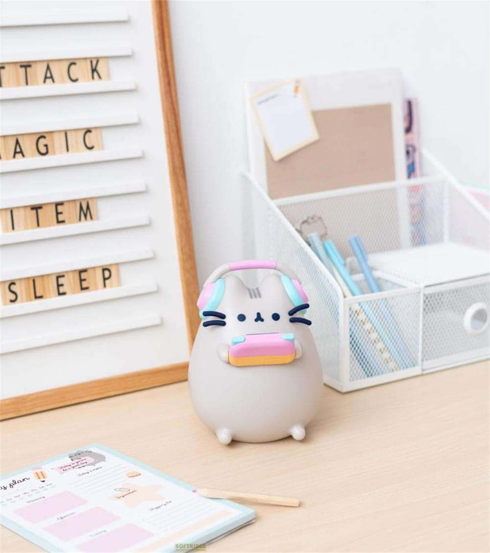 Graue Figur einer Katze mit Kopfhörern und einem Spielgerät auf einem Schreibtisch.