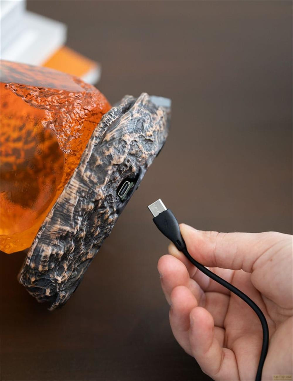 Mano inserta cable USB-C en objeto naranja texturizado como piedra.