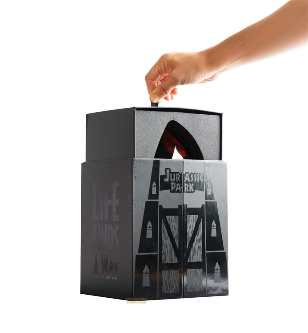 Una mano abre una caja negra con el logo de "Jurassic Park" y el texto "Life Finds A Way".