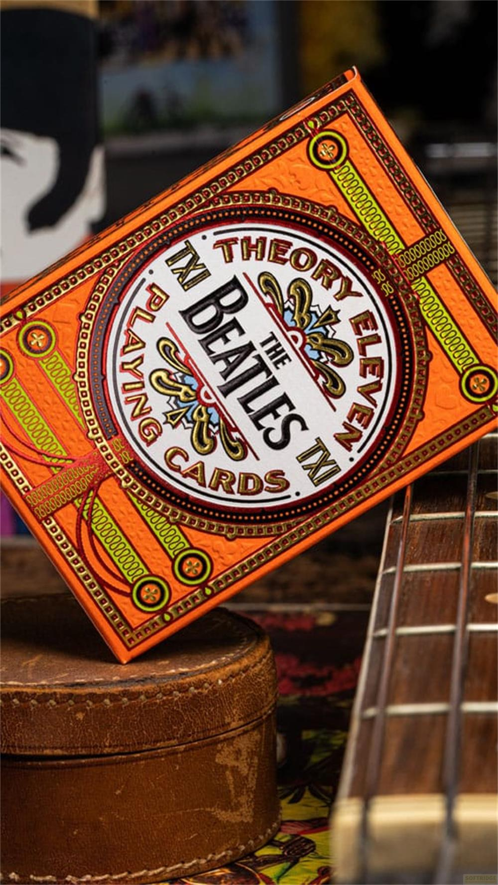 Scatola arancione di carte da gioco Beatles su una custodia in pelle accanto a una chitarra.