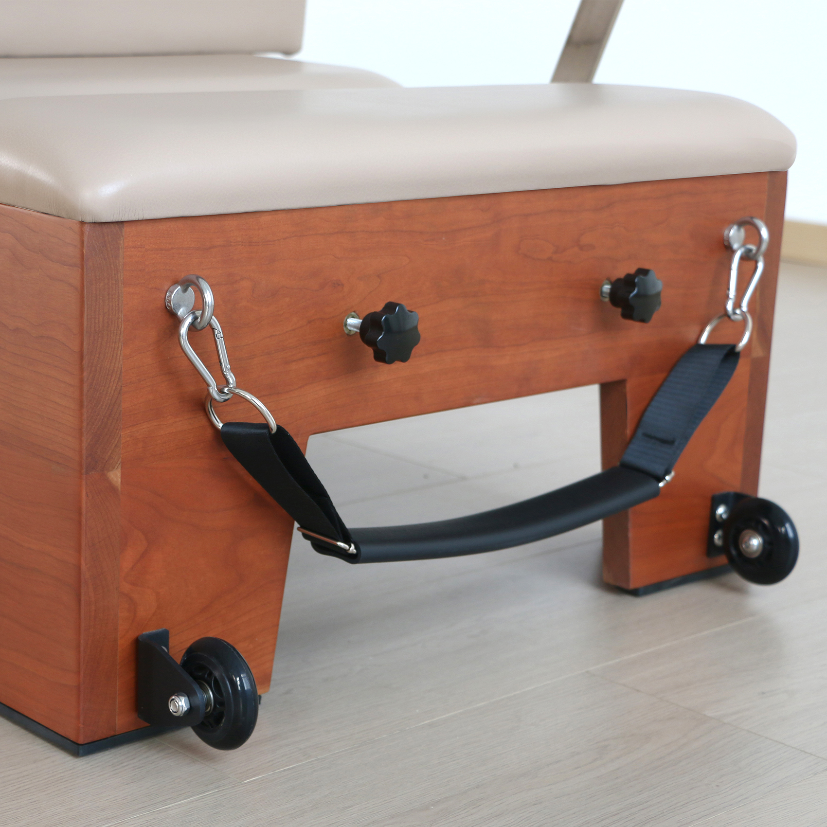 Riformatore Pilates in legno con tappezzeria beige, ruote e cinghia nera.