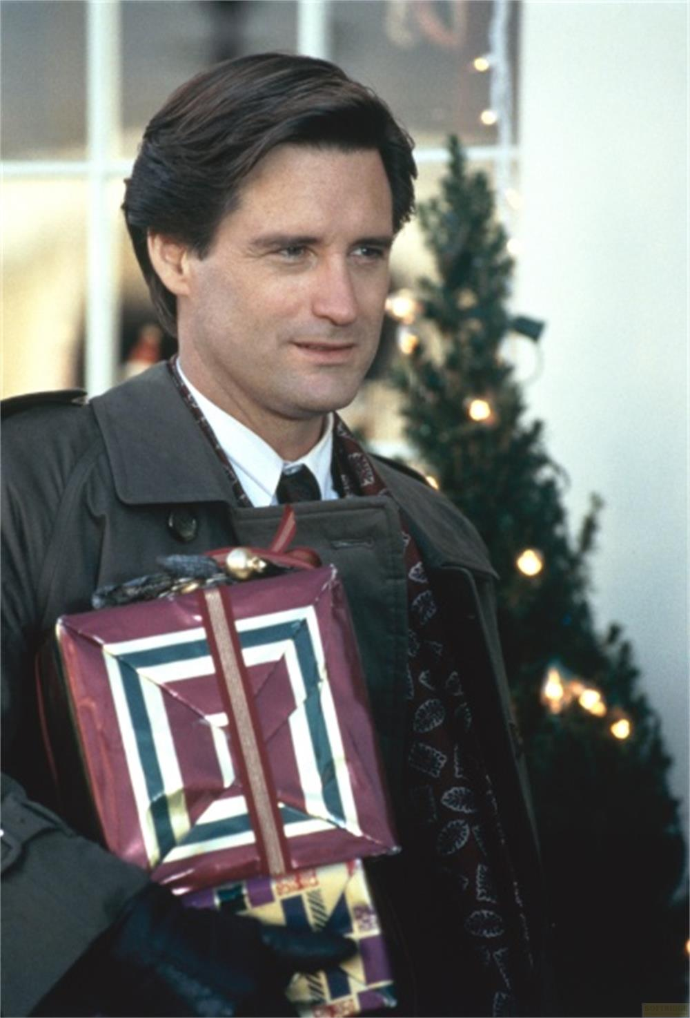 Homme tenant des cadeaux devant un sapin de Noël.