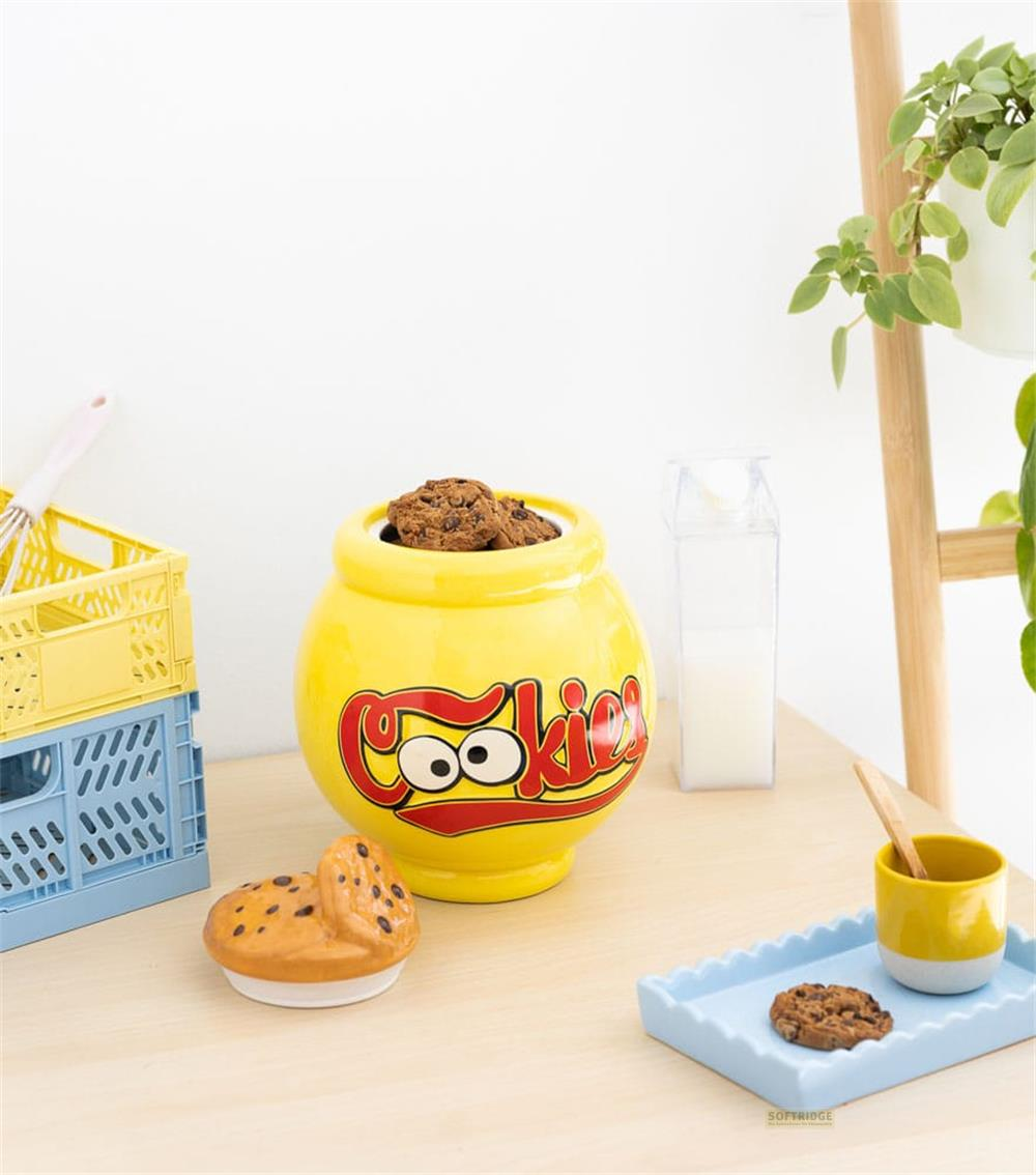 Tarro de galletas amarillo con texto, una galleta y un vaso de leche al lado.