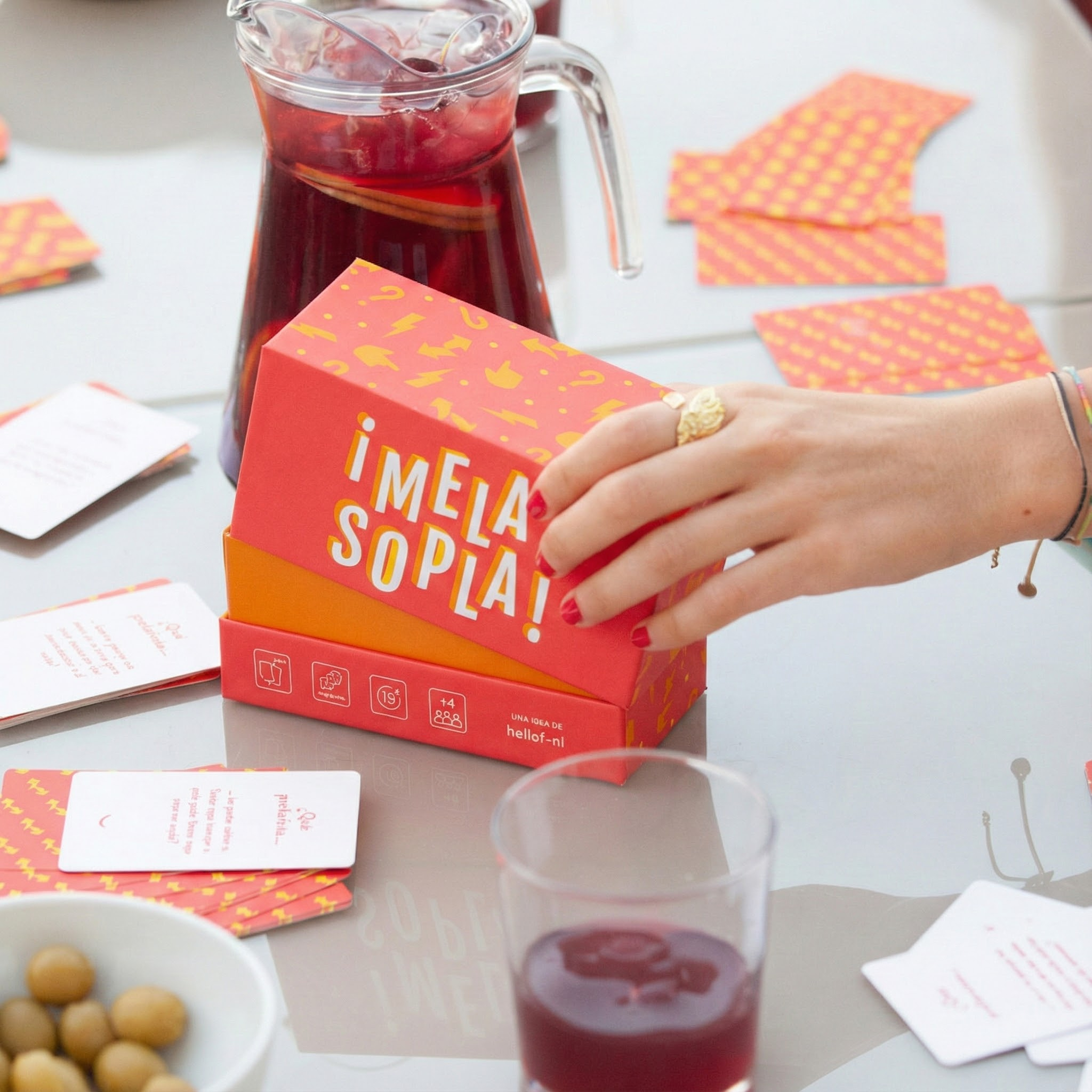 Una caja de juego roja con símbolos amarillos, junto a una jarra de bebida roja.