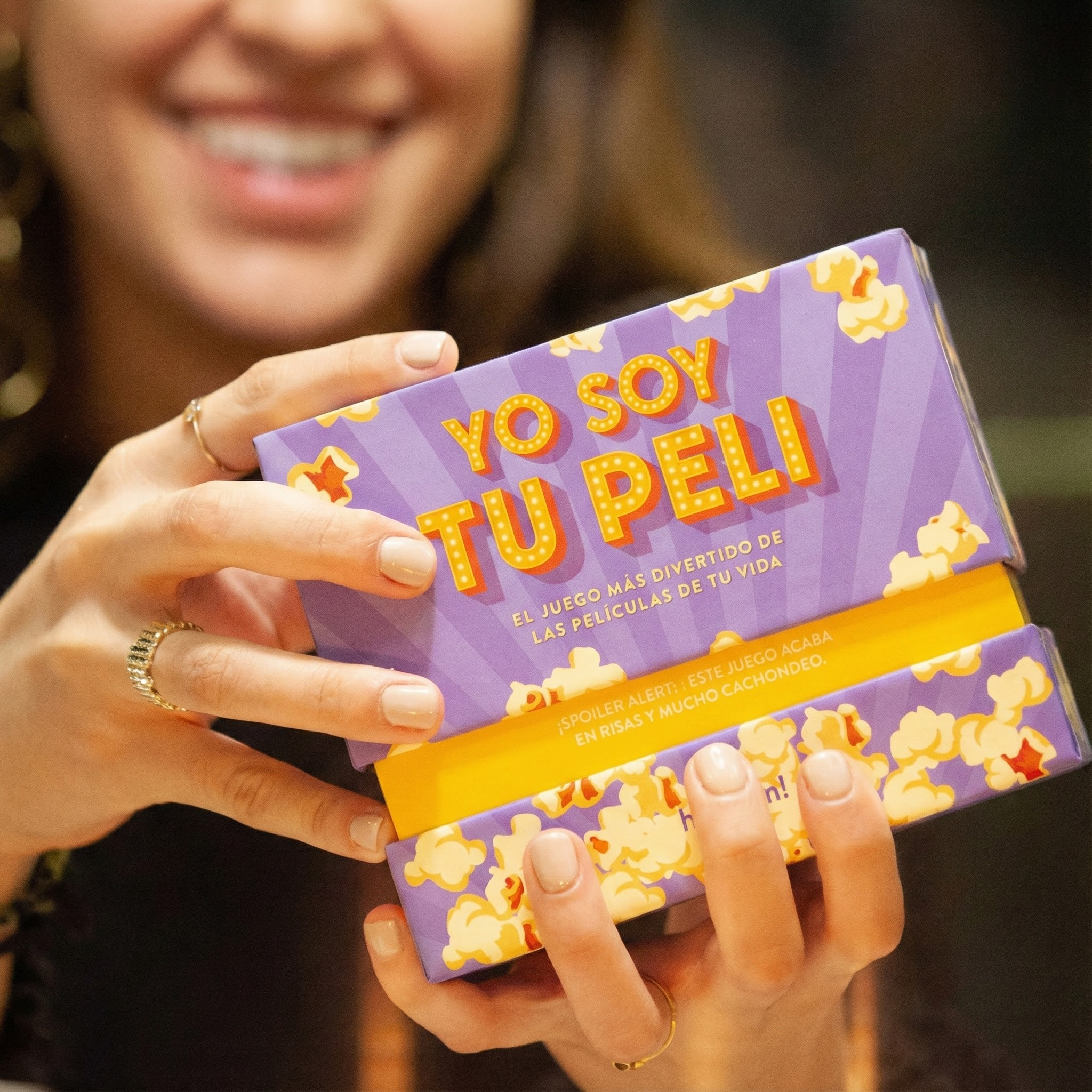 Una persona sostiene una caja morada con motivos de palomitas y el texto "YO SOY TU PELI".
