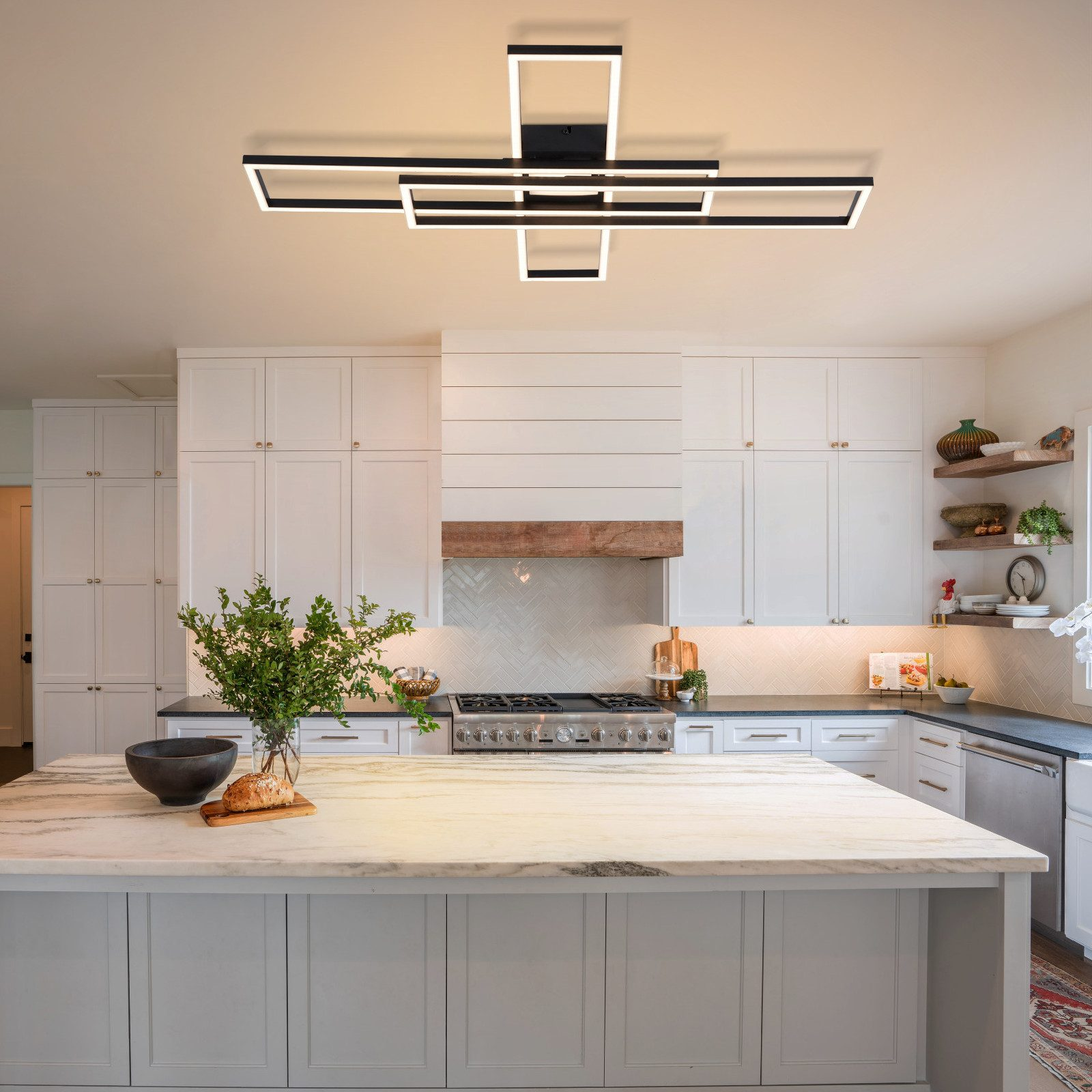 Cucina moderna con mobili bianchi, isola in marmo, piano cottura a gas e lampada da soffitto geometrica.