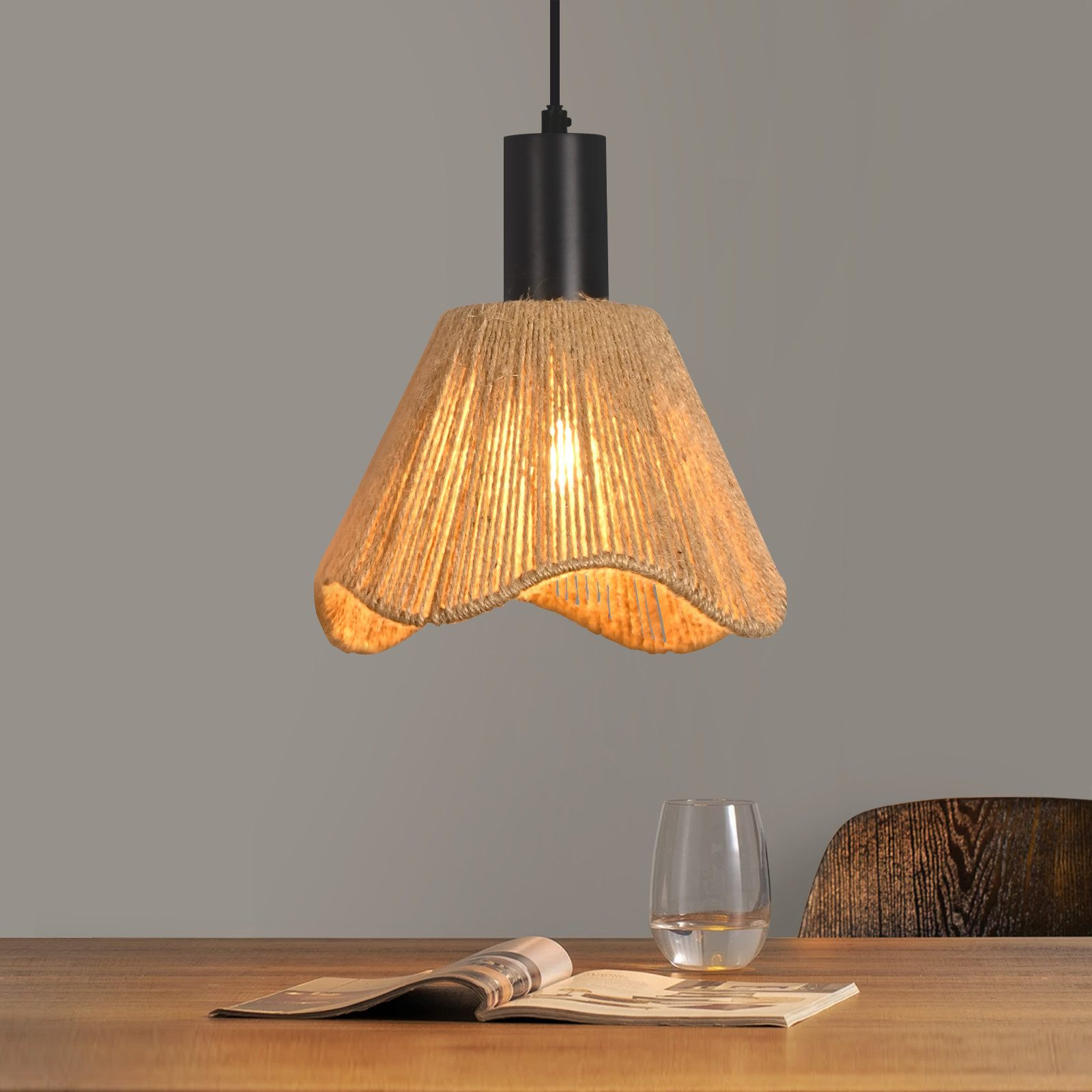 Una lampada a sospensione in juta appesa sopra un tavolo di legno con una rivista e un bicchiere d'acqua.