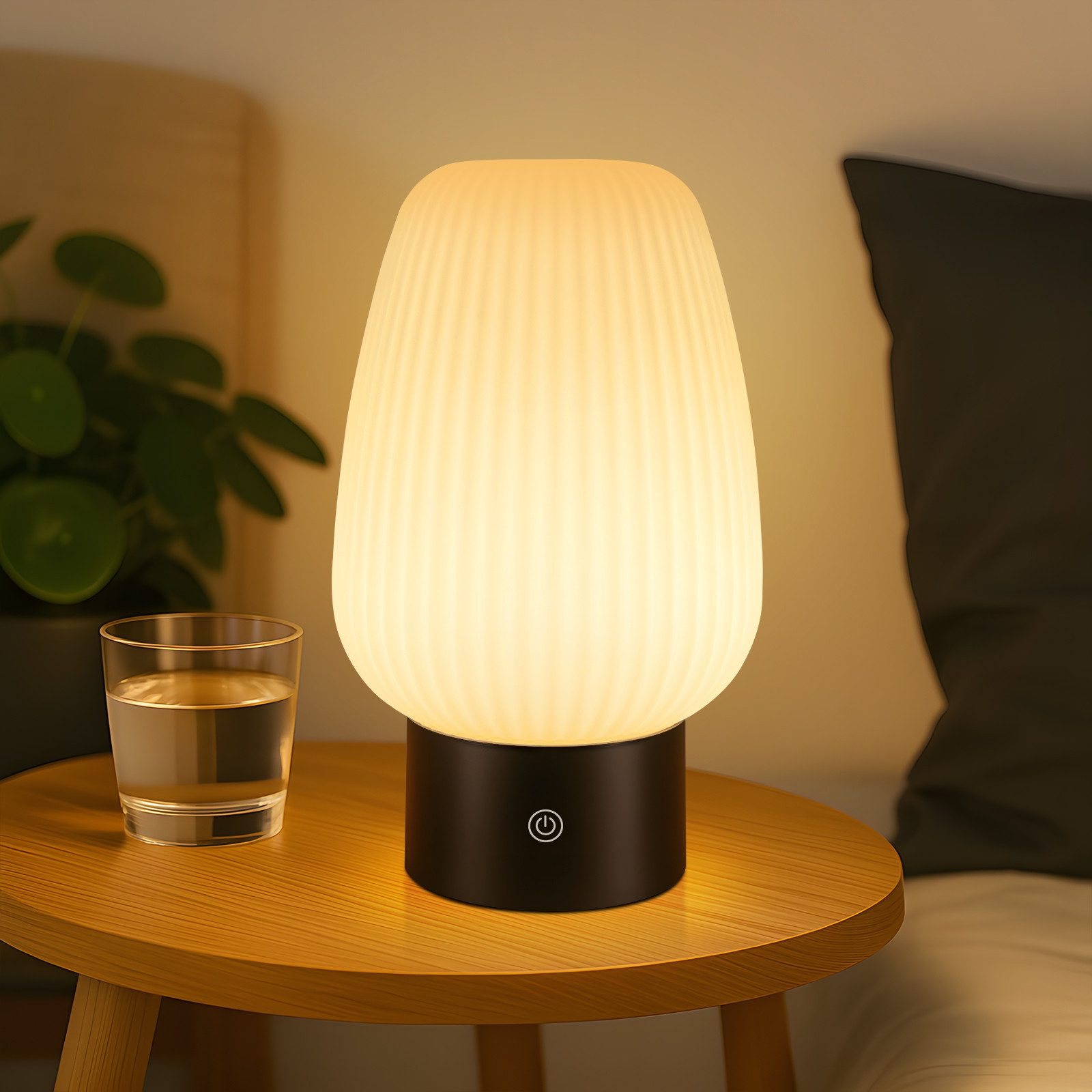 Una lampada da comodino con paralume a coste brilla su un tavolo di legno accanto a un bicchiere d'acqua.