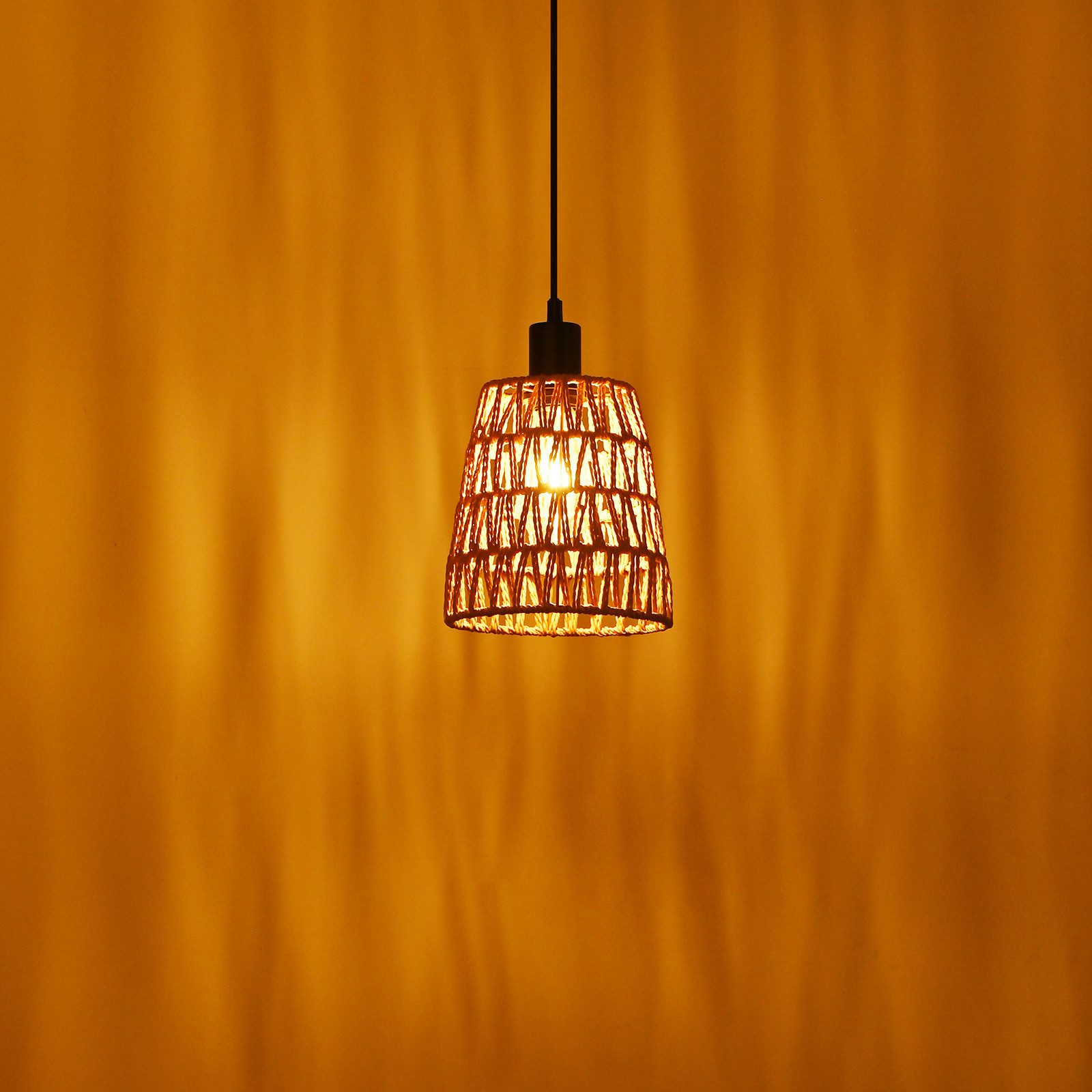 Hängende Lampe mit geflochtenem Schirm vor orangefarbener Wand mit Schatten.