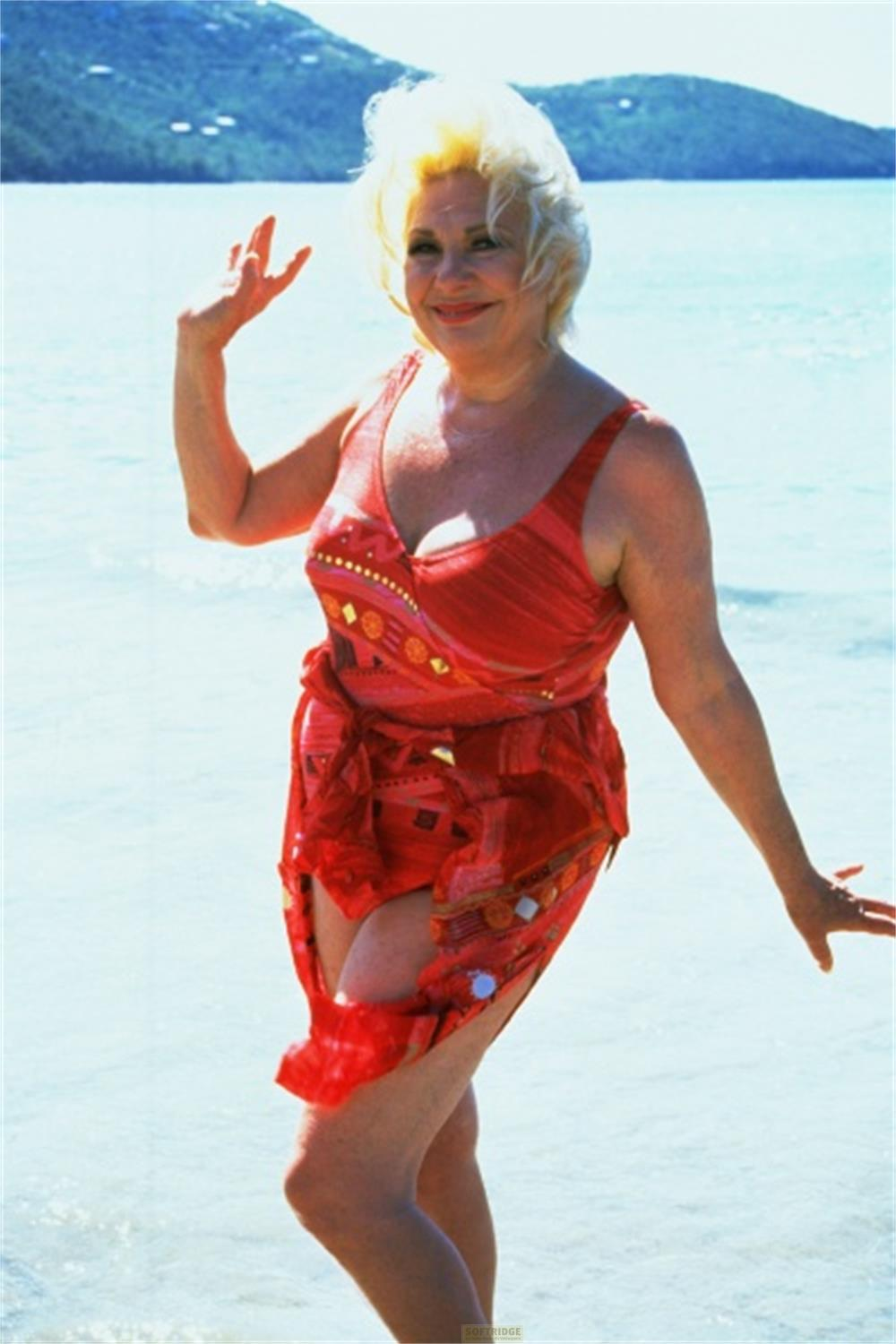 Una donna in costume rosso saluta sulla spiaggia.