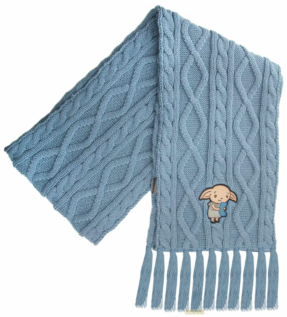 Ein hellblauer Strickschal mit Zopfmuster und einem kleinen Kobold-Aufnäher.